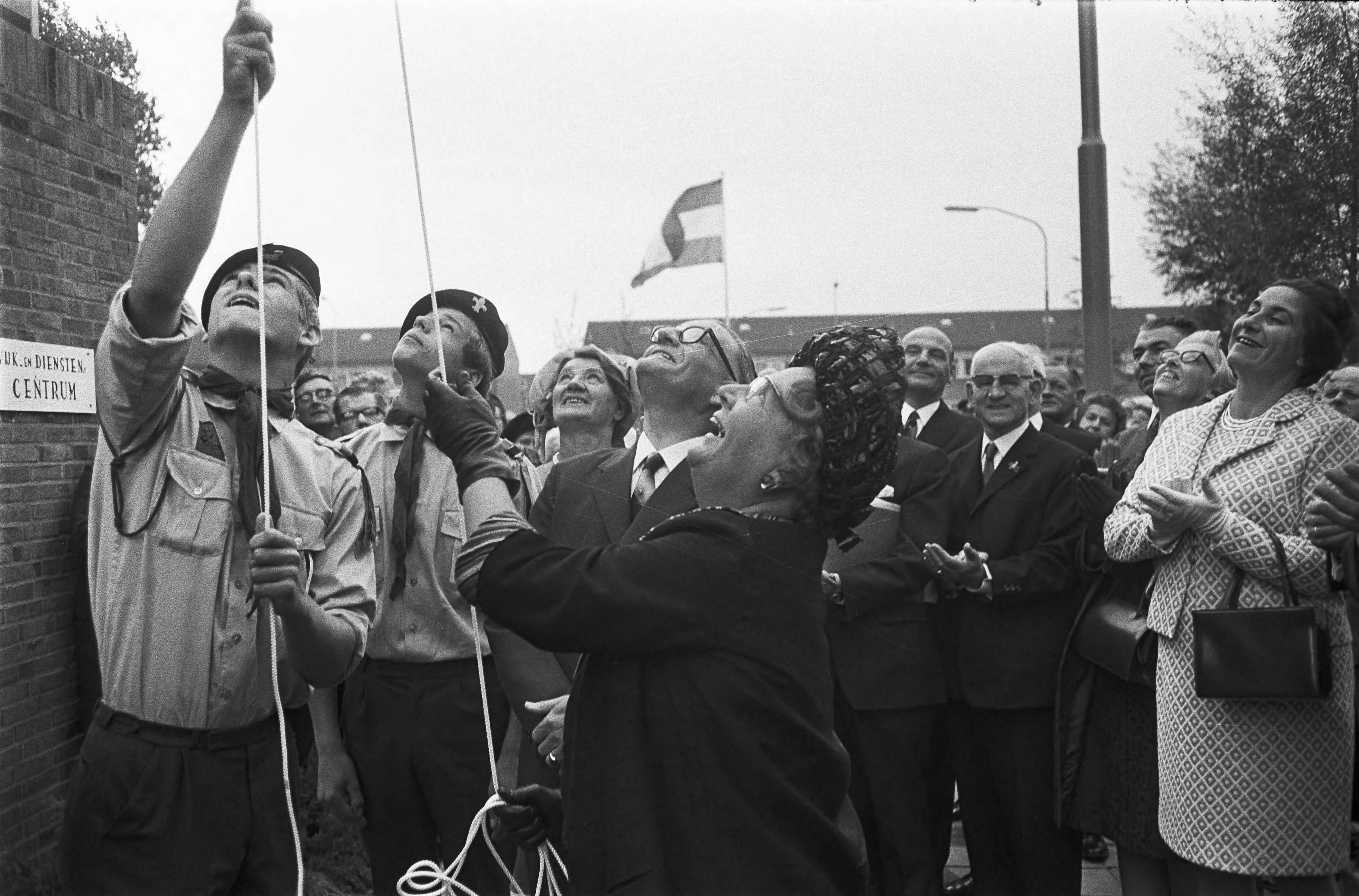 Koningin Juliana bezoekt Oost-Groningen — Koningin Juliana opent het bejaardencentrum "De Reensche Compagnie" in Hoogezand door de vlag te hijsen — Foto: Fotograaf Onbekend / Anefo. Licentie: Set B: Rechtenvrij / Publiek Domein. Bron: Nationaal Archief. http://hdl.handle.net/10648/ab7c35cc-d0b4-102d-bcf8-003048976d84