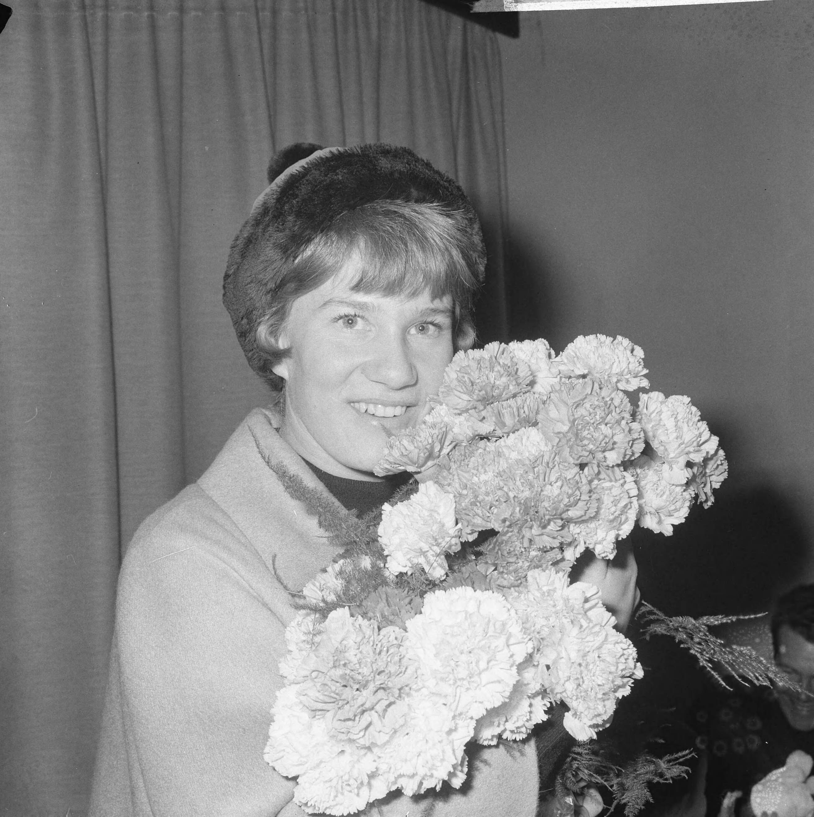 Aankomst van Sjoukje Dijkstra op Schiphol voor een optreden bij Holiday on Ice — Sjoukje terwijl ze een bos bloemen vasthoudt — Foto: Nijs, Jac. de / Anefo. Licentie: Set B: Rechtenvrij / Publiek Domein. Bron: Nationaal Archief. http://hdl.handle.net/10648/aac9db3e-d0b4-102d-bcf8-003048976d84