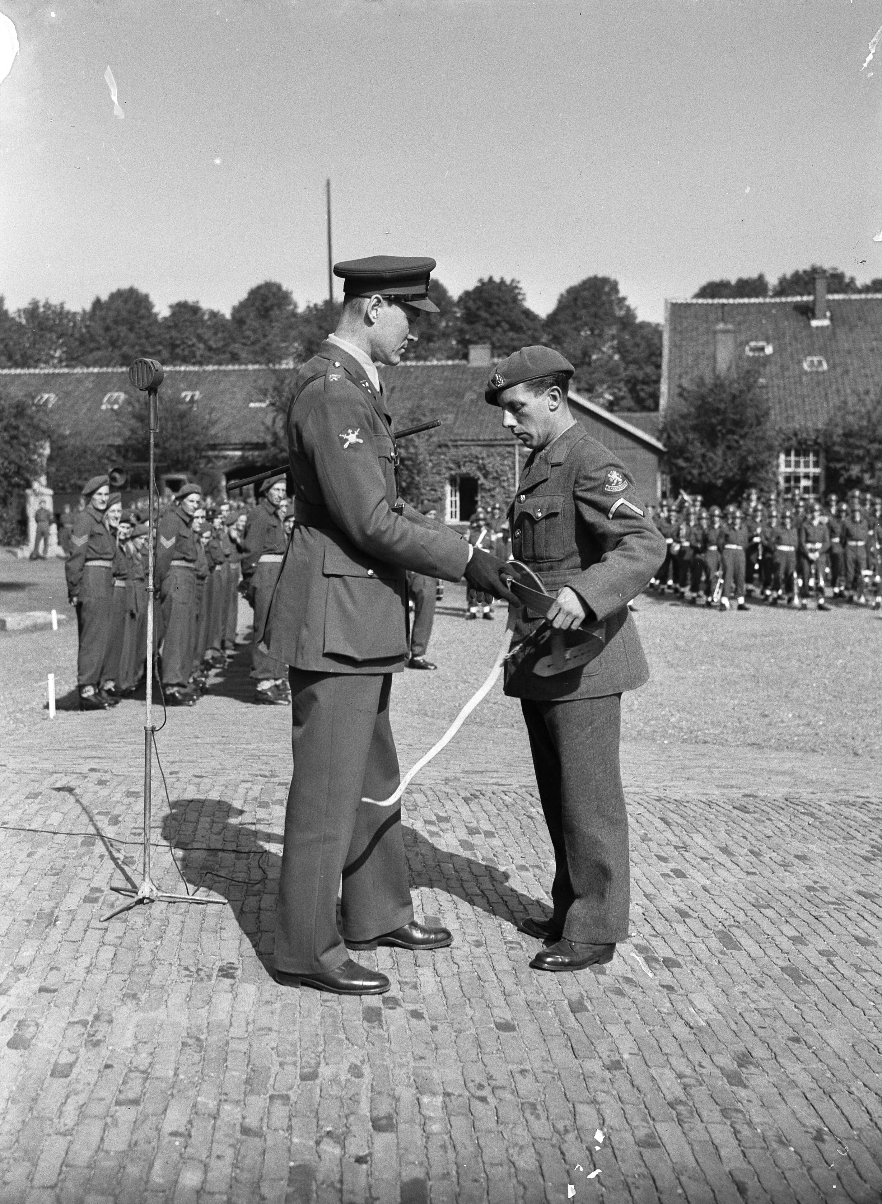 Fotocollectie Anefo — Afscheidsparade opleidingscursus Reserve-officieren Breda. Op een paradeplaats van een kazerne reikt een kolonel een bandelier [draagriem voor vlag] uit aan een korporaal — Foto: Sagers, Harry / Anefo. Licentie: Set B: Rechtenvrij / Publiek Domein. Bron: Nationaal Archief. http://hdl.handle.net/10648/a8acfbb0-d0b4-102d-bcf8-003048976d84