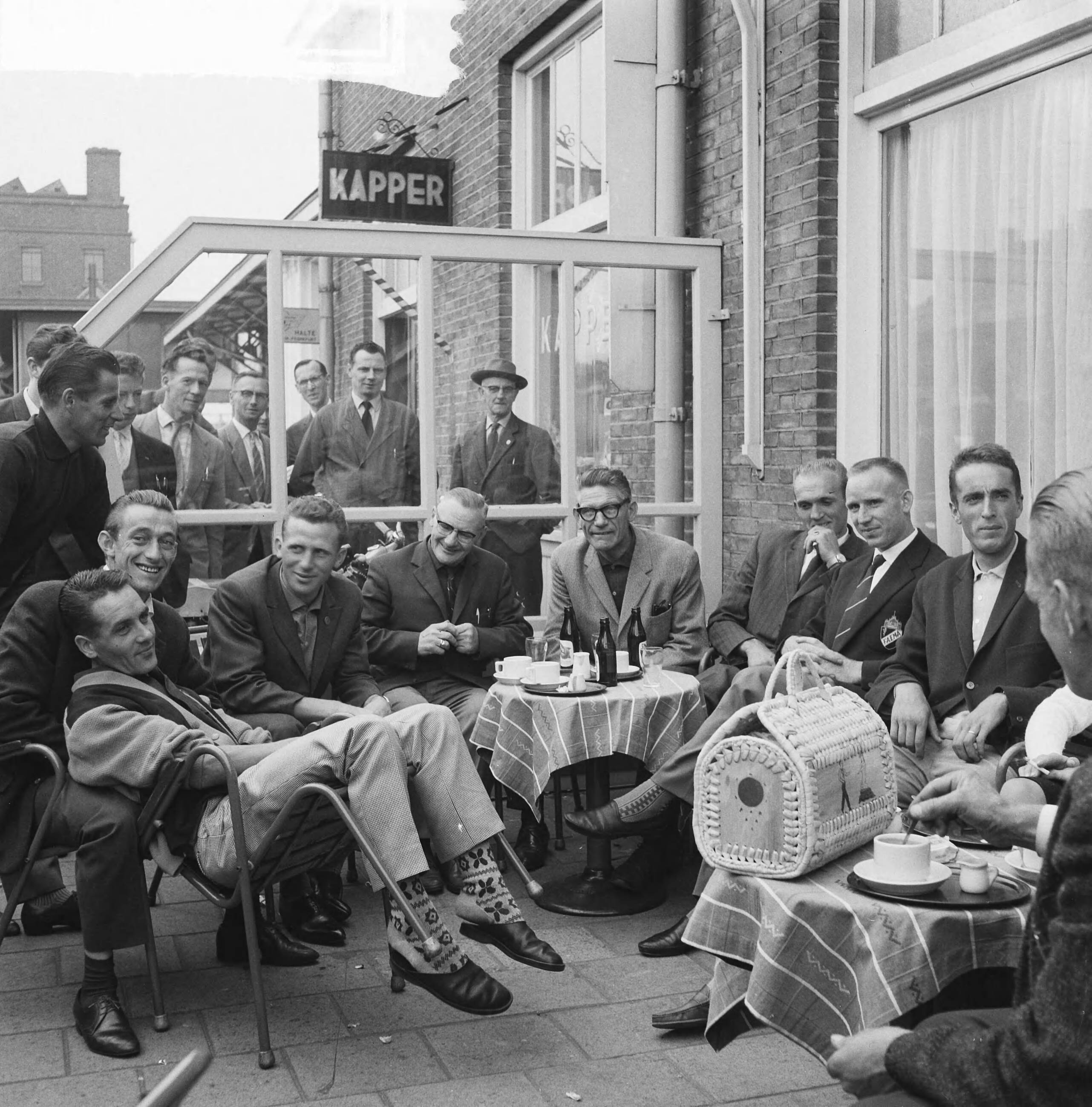 Tour de France 1961 — Vertrek Tour de France ploeg naar Frankrijk. De renners en officials op het terras. Zittend vlnr. Piet Damen, Wout Wagtmans, Jaap Kersten, verzorger, ploegleider Klaas Buchly, Coen Niesten, Piet van Est en Ab Geldermans — Foto: Koch, Eric / Anefo. Licentie: Set B: Rechtenvrij / Publiek Domein. Bron: Nationaal Archief. http://hdl.handle.net/10648/a9d9a344-d0b4-102d-bcf8-003048976d84