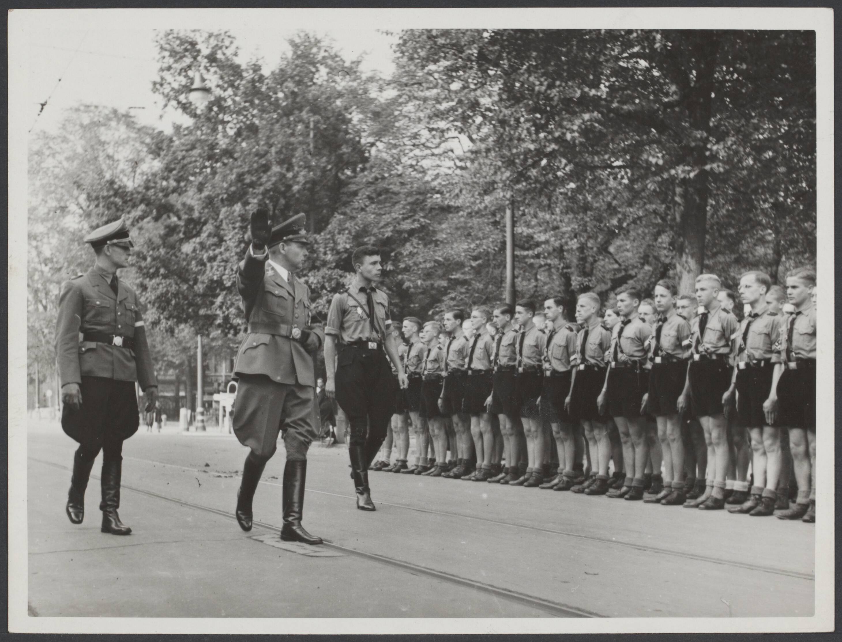 Nederland '40/'45. Organisaties behalve Winterhulp. — Op plechtige wijze vond op zondag in de Stadsschouwburg te Den Haag de opname der 19-jarigen der "HJ" [Hitlerjugend] in de "NSDAP" door Hauptdienstleiter Schmidt plaats. Bij zijn aankomst inspecteerde hij een aangetreden ereformatie — Foto: Stapf Bilderdienst. Licentie: Set B: Rechtenvrij / Publiek Domein. Bron: Nationaal Archief. http://hdl.handle.net/10648/870cec7f-8847-60aa-b3a3-30398d2b54eb
