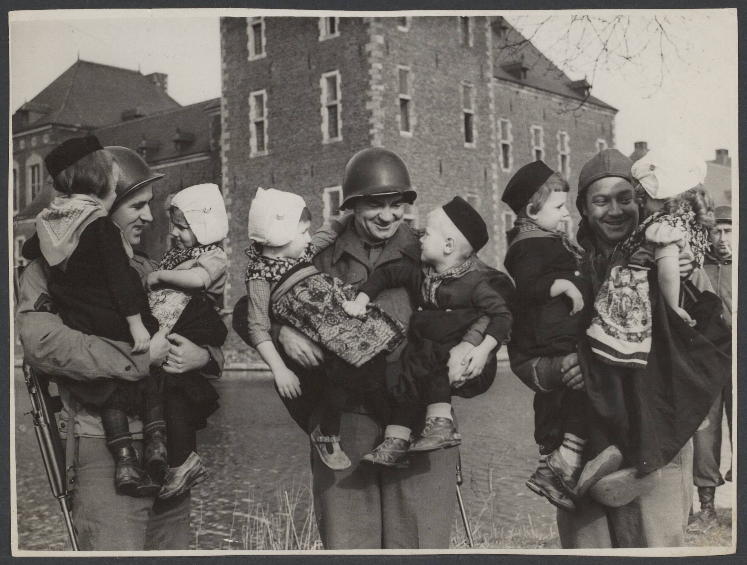 Bevrijding Nederland 1944 [bevat ook foto's uit 1945] — Kasteel Hoensbroek huist 145 Nederlandse kinderen die verzorgd worden door nonnen. Amerikaanse G.I. 's die in de buurt gelegerd zijn assisteren de nonnen door wandelingen te maken met deze driejarige kinderen, die in klederdracht gestoken zijn. Vlnr. Walter Ward uit Newark, Thomas McMorrow uit Brooklyn en James Firman uit Delaware (Ohio) — Foto: Keystone Press / Rechtenvrij. Licentie: Set B: Rechtenvrij / Publiek Domein. Bron: Nationaal Archief. http://hdl.handle.net/10648/2b481ad1-c271-dfcb-53dd-0d890a4a09c9