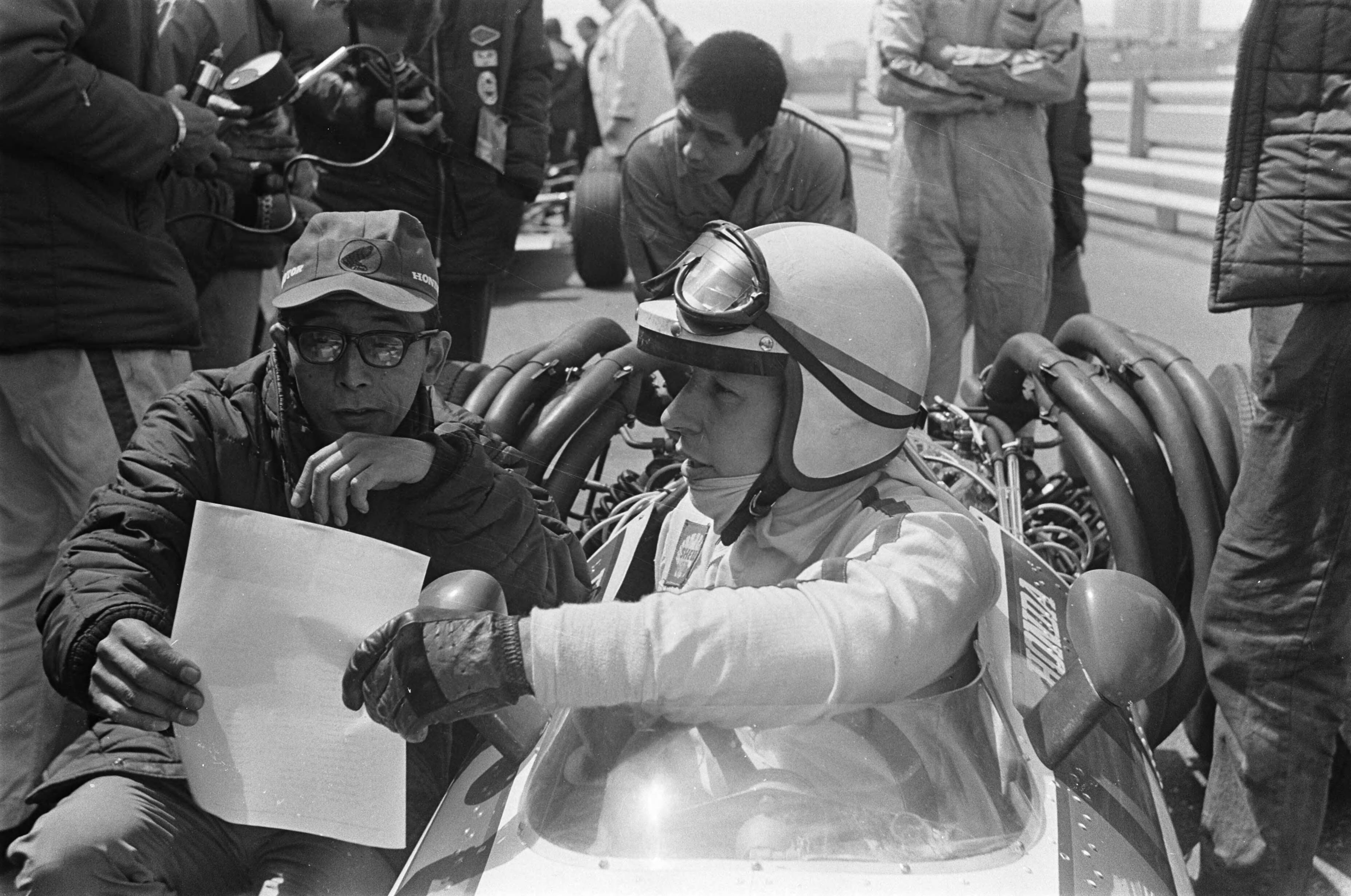 Fotocollectie Anefo — Grand Prix 68 Zandvoort training. John Surtees in bespreking met de Honda renstalleider — Foto: Evers, Joost / Anefo. Licentie: Set B: Rechtenvrij / Publiek Domein. Bron: Nationaal Archief. http://hdl.handle.net/10648/ab44b9bc-d0b4-102d-bcf8-003048976d84