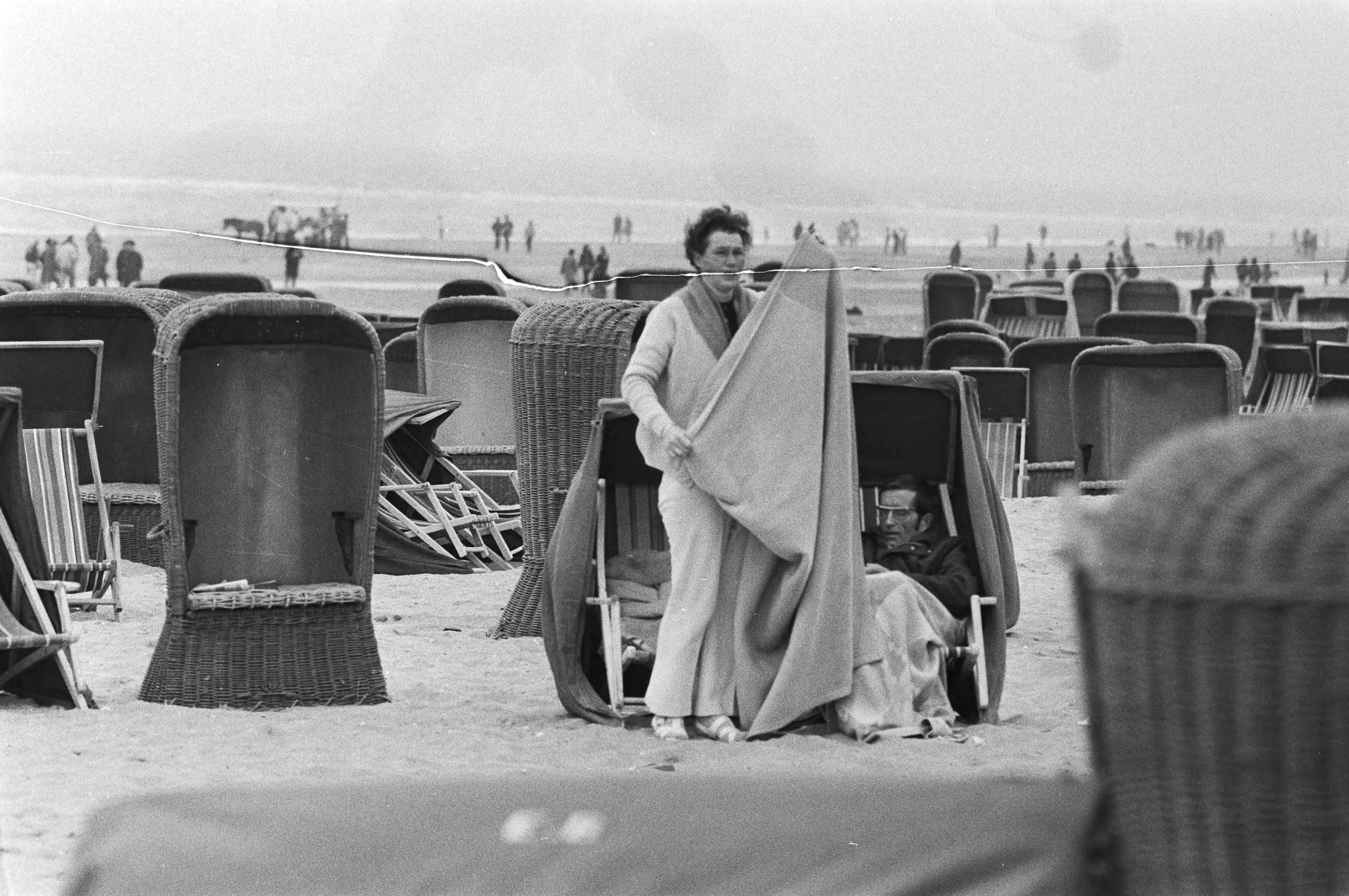 Zandvoort — Mensen in dikke kleding in een strandstoel — Foto: Fotograaf Onbekend / Anefo. Licentie: Set B: Rechtenvrij / Publiek Domein. Bron: Nationaal Archief. http://hdl.handle.net/10648/abbaf348-d0b4-102d-bcf8-003048976d84