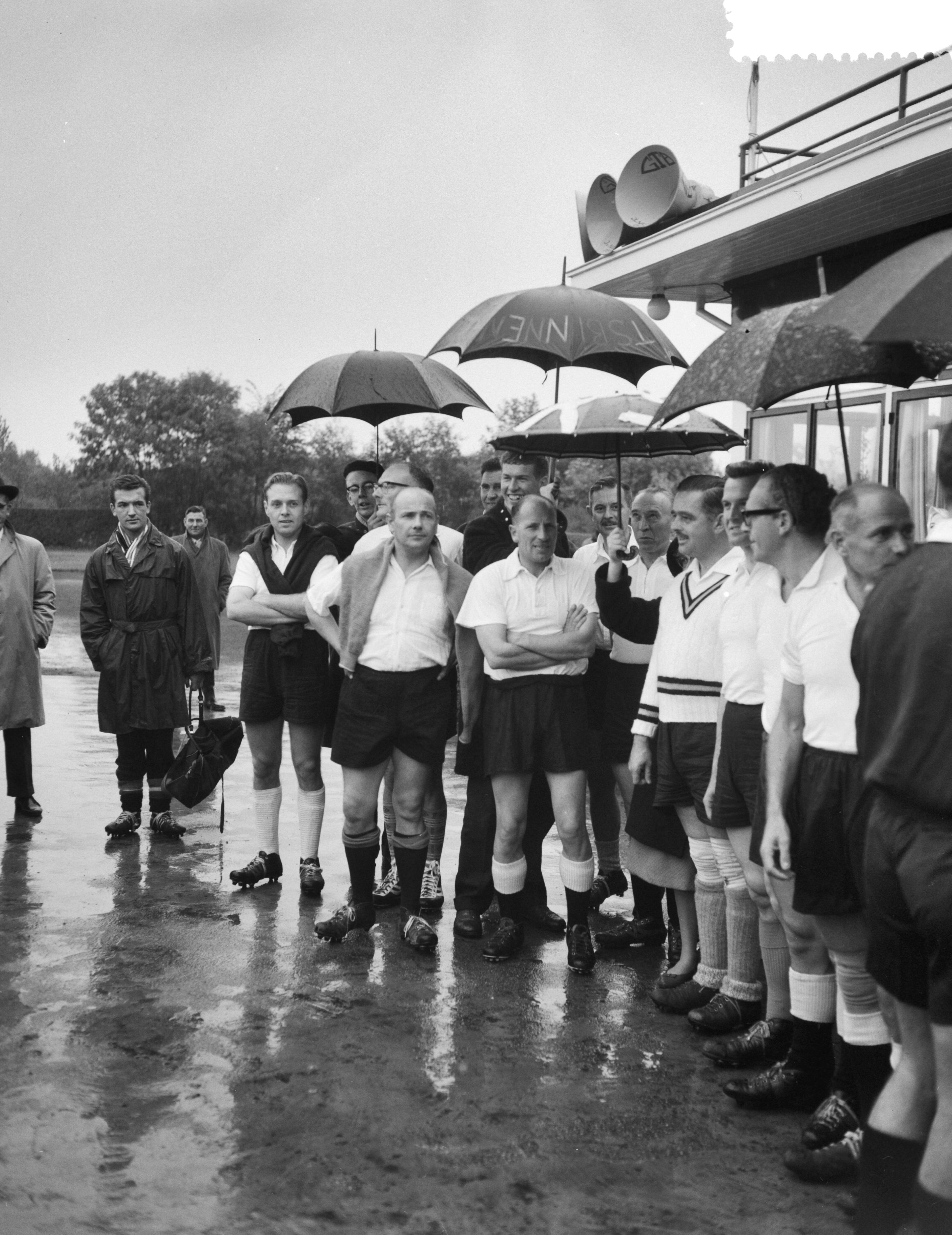 Fotocollectie Anefo — Interparlementair voetbal. Holland tegen België op sportpark Te Werve in Rijswijk. Aanhangers houden de spelers droog — Foto: Rossem, Wim van / Anefo. Licentie: Set B: Rechtenvrij / Publiek Domein. Bron: Nationaal Archief. http://hdl.handle.net/10648/a99fffd6-d0b4-102d-bcf8-003048976d84