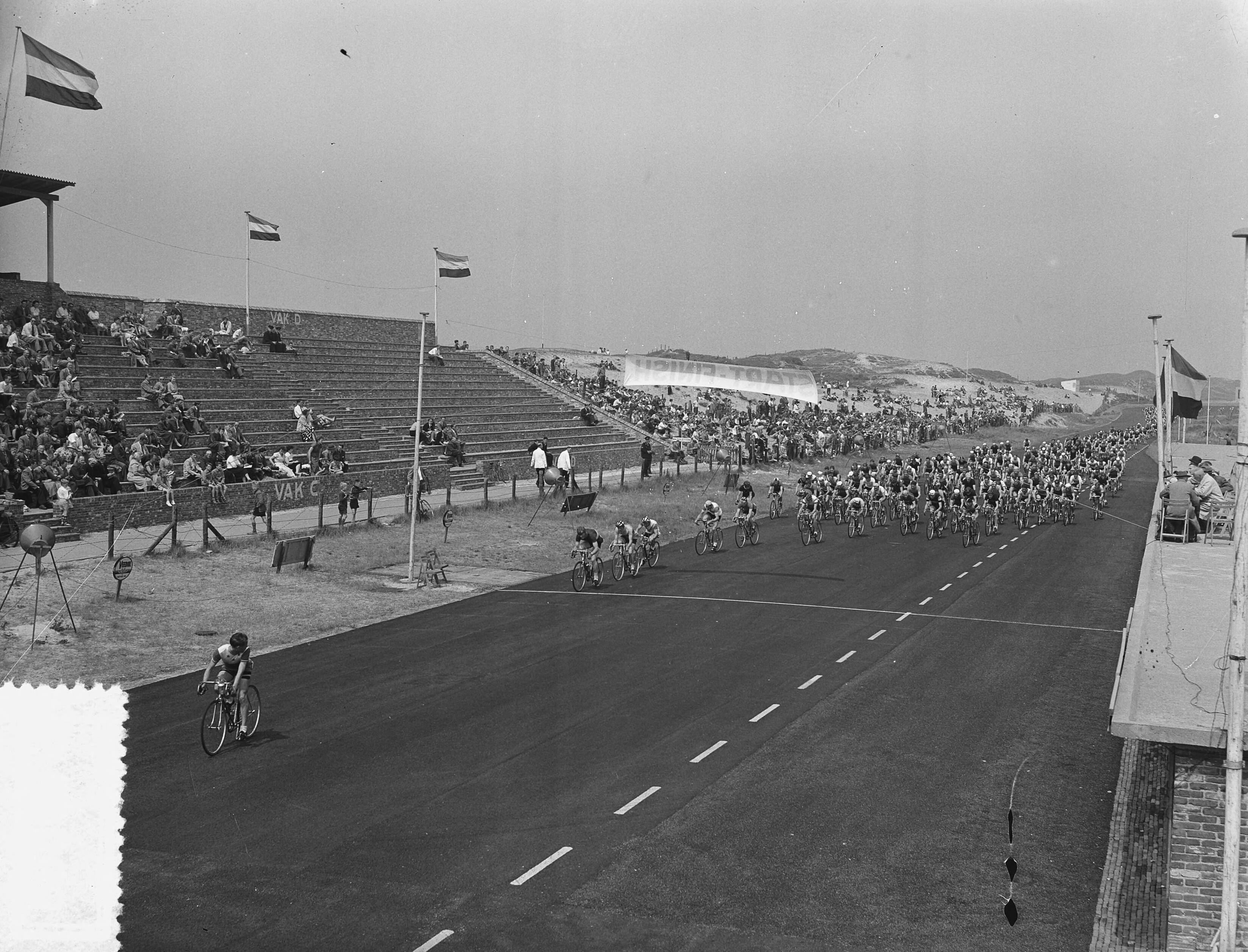 Fotocollectie Anefo — Nederlands kampioenschap wielrennen op de weg voor amateurs op het circuit van Zandvoort. Tijdens de rit — Foto: Fotograaf Onbekend / Anefo. Licentie: Set B: Rechtenvrij / Publiek Domein. Bron: Nationaal Archief. http://hdl.handle.net/10648/a92596a6-d0b4-102d-bcf8-003048976d84