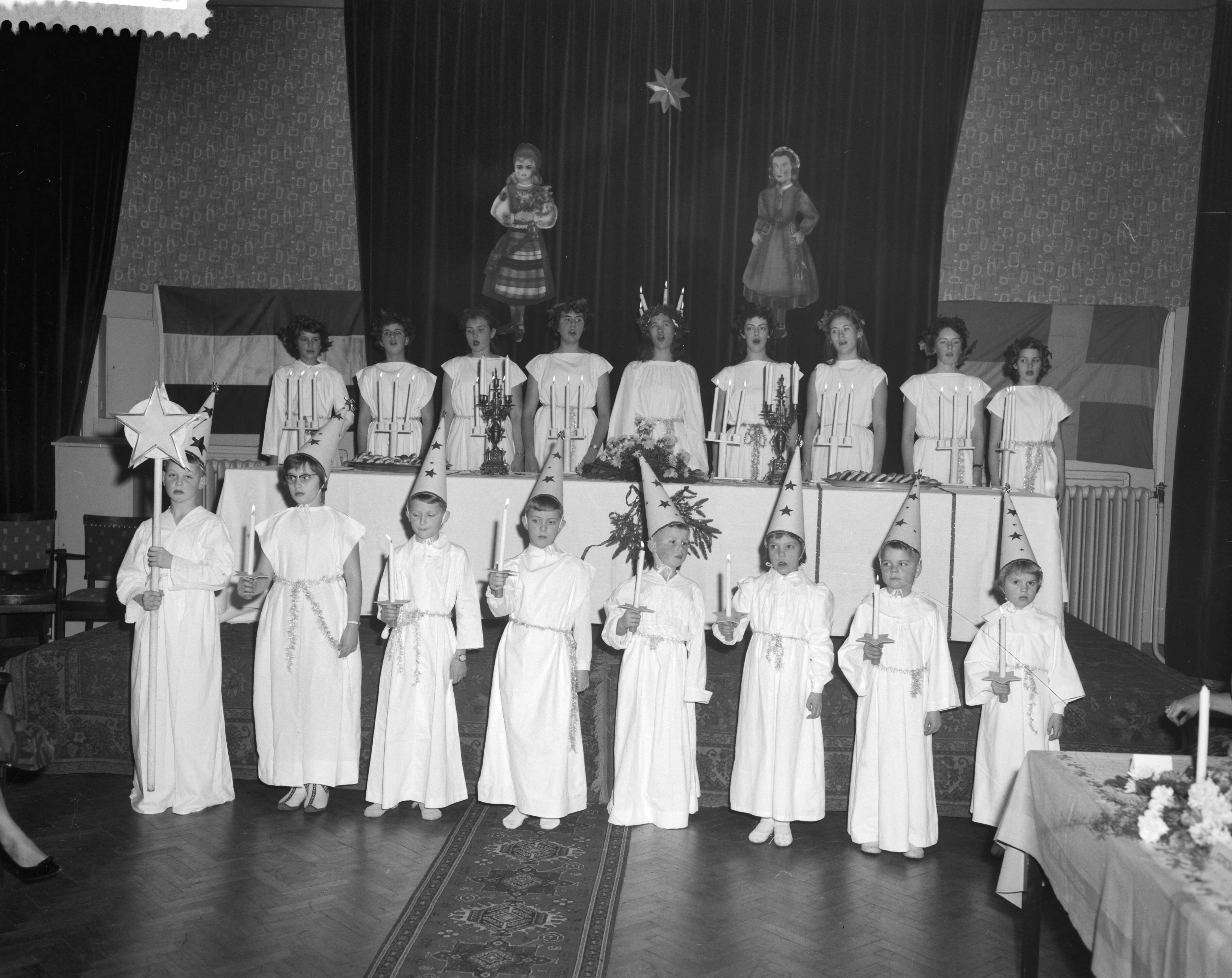 Fotocollectie Anefo — Viering van het Luciafeest door de Zweeds Nederlandse Vereniging in de Dierentuin te Den Haag , in het midden Lucia, de 18-jarige Helbertijn Küller uit Den Haag temidden van de "ternin". Voor haar de "sterrejongens" — Foto: Behrens, Herbert F. / Anefo. Licentie: Set B: Rechtenvrij / Publiek Domein. Bron: Nationaal Archief. http://hdl.handle.net/10648/a9a3ae06-d0b4-102d-bcf8-003048976d84