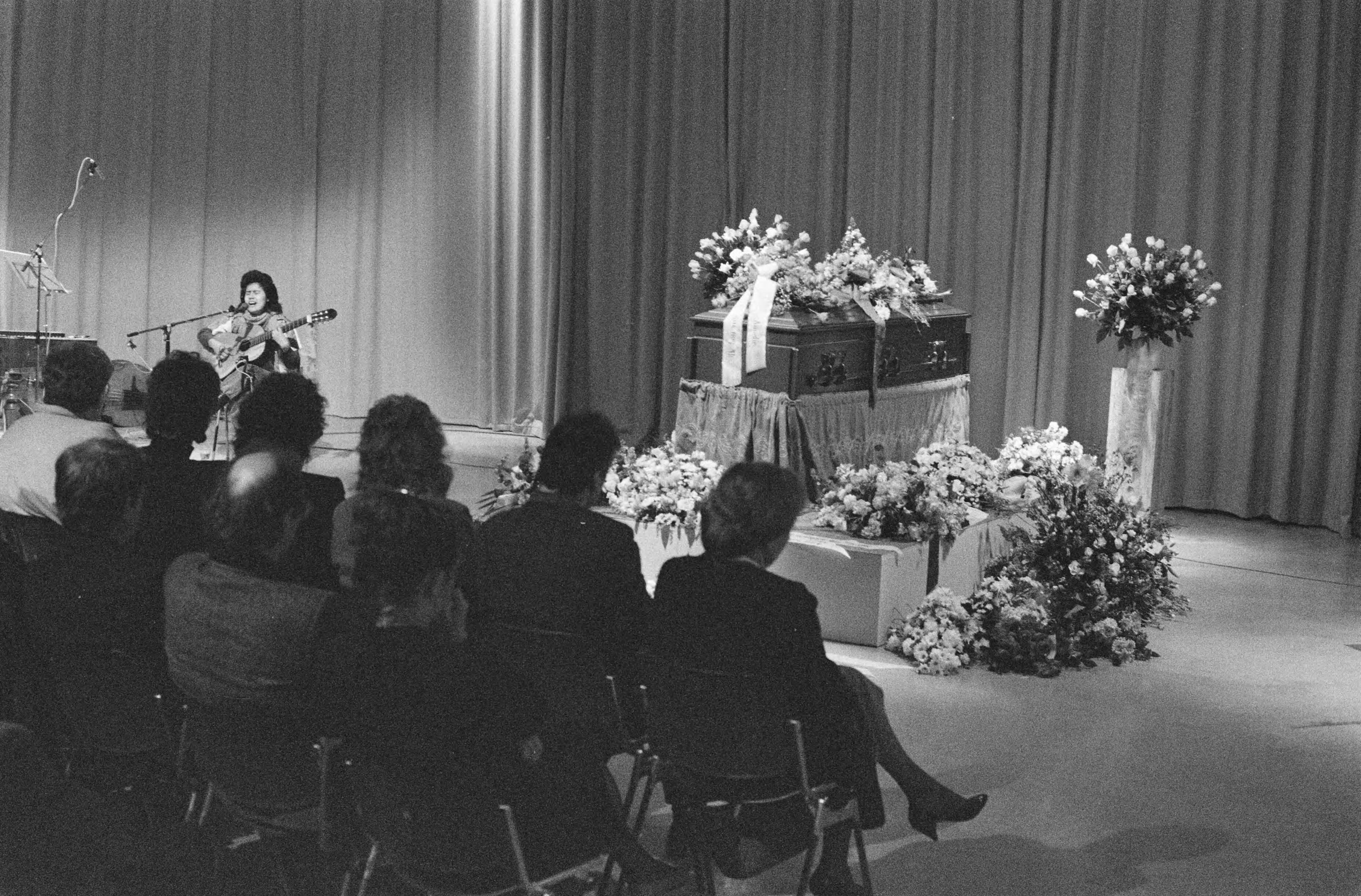 Herdenkingsdienst voor de doodgeschoten cameraman Cornel Lagrouw in Hilversum — Aanwezigen zitten in de ruimte waar de kist met bloemen staat — Foto: Bogaerts, Rob / Anefo. Licentie: Set B: Rechtenvrij / Publiek Domein. Bron: Nationaal Archief. http://hdl.handle.net/10648/ad71d332-d0b4-102d-bcf8-003048976d84