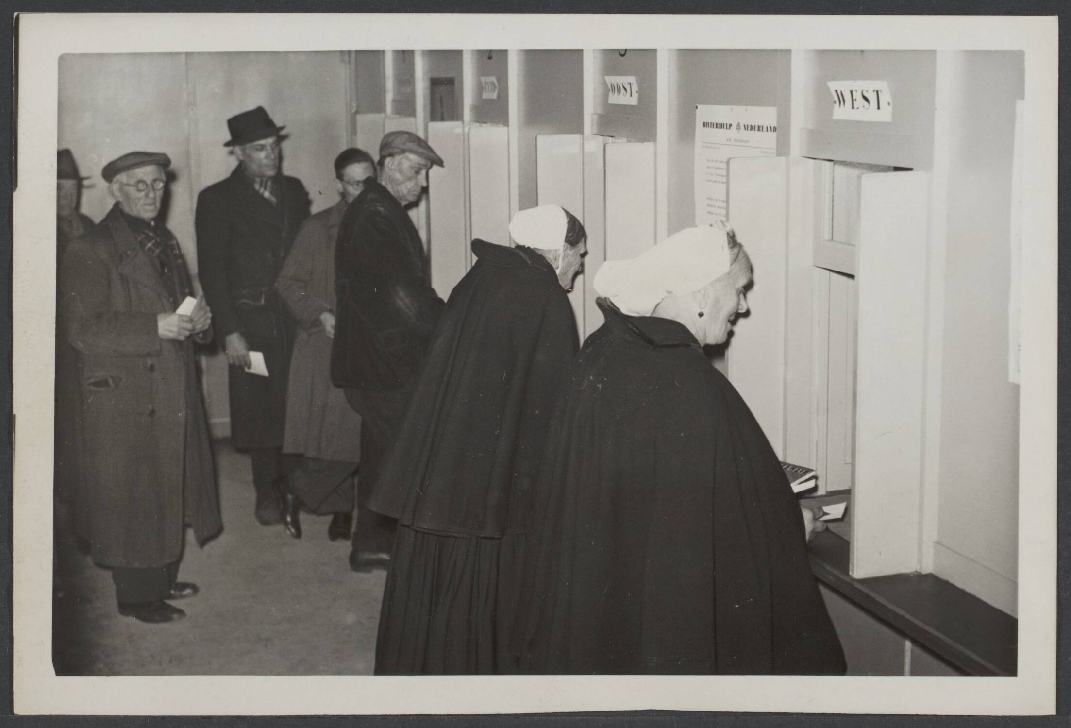 Winterhulp — Winterhulp Nederland is begonnen met de uitgifte van de waardebonnen voor het seizoen 1941. Scheveningse vrouwen nemen de bonnen op het bureau van de W.H.N. in Den Haag in ontvangst — Foto: Meijer, T.A. / N.V. Polygoon (1). Licentie: Set B: Rechtenvrij / Publiek Domein. Bron: Nationaal Archief. http://hdl.handle.net/10648/6bb6bbcd-dd59-6e49-eddb-f1fa7f065805