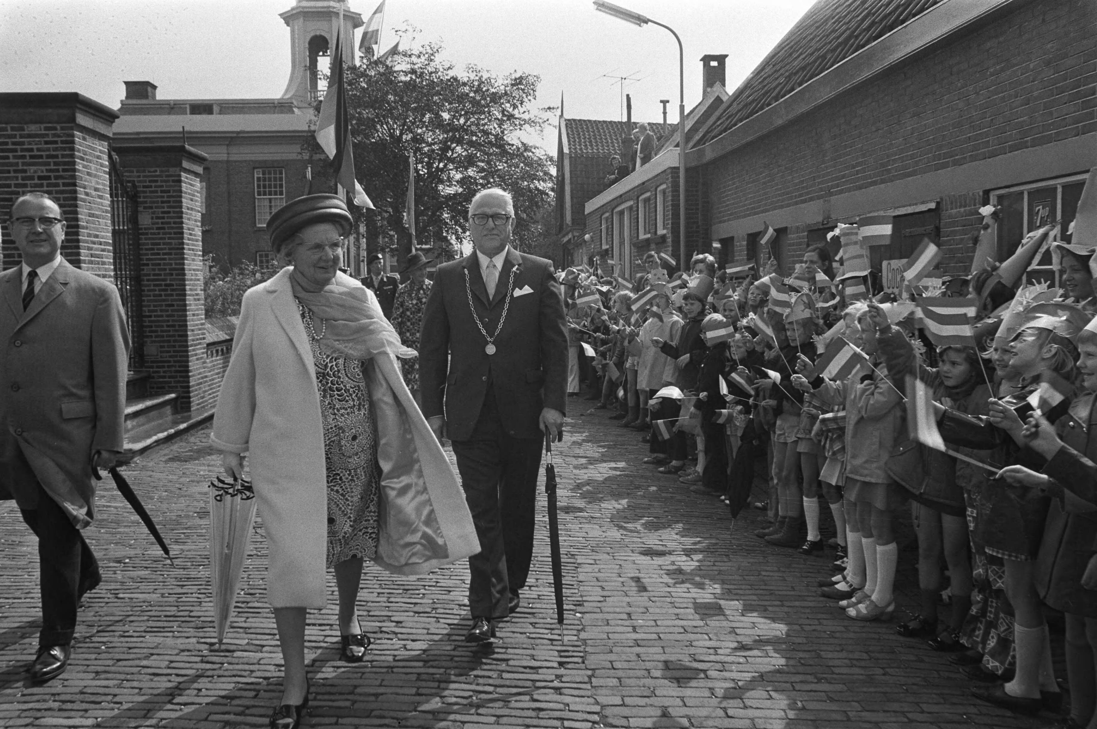 Koningin Juliana op bezoek in de Zaanstreek — Koningin Juliana tijdens de wandeling door Westzaan, in gezelschap van burgemeester van Westzaan, Frederik Verstegen (r.) en de Commissaris van de Koningin in Zuid-Holland, mr. F.J. Kranenburg — Foto: Fotograaf Onbekend / Anefo. Licentie: Set B: Rechtenvrij / Publiek Domein. Bron: Nationaal Archief. http://hdl.handle.net/10648/abec13ba-d0b4-102d-bcf8-003048976d84