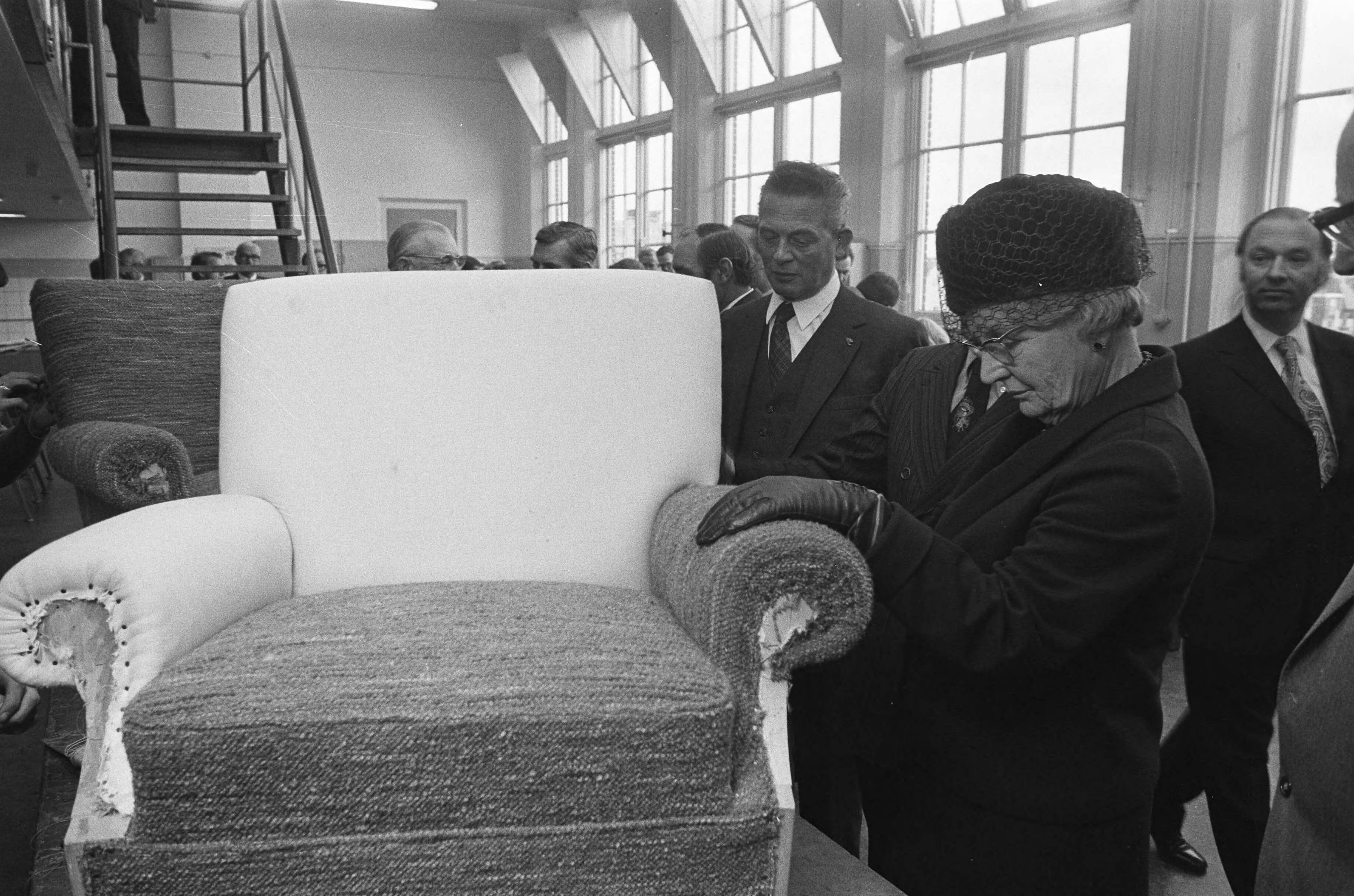 Koningin Juliana bezoekt scholen in Den Haag — De koningin bekijkt de stoffering van een stoel in een van de bezochte scholen — Foto: Fotograaf Onbekend / Anefo. Licentie: Set B: Rechtenvrij / Publiek Domein. Bron: Nationaal Archief. http://hdl.handle.net/10648/ac3c3cc8-d0b4-102d-bcf8-003048976d84