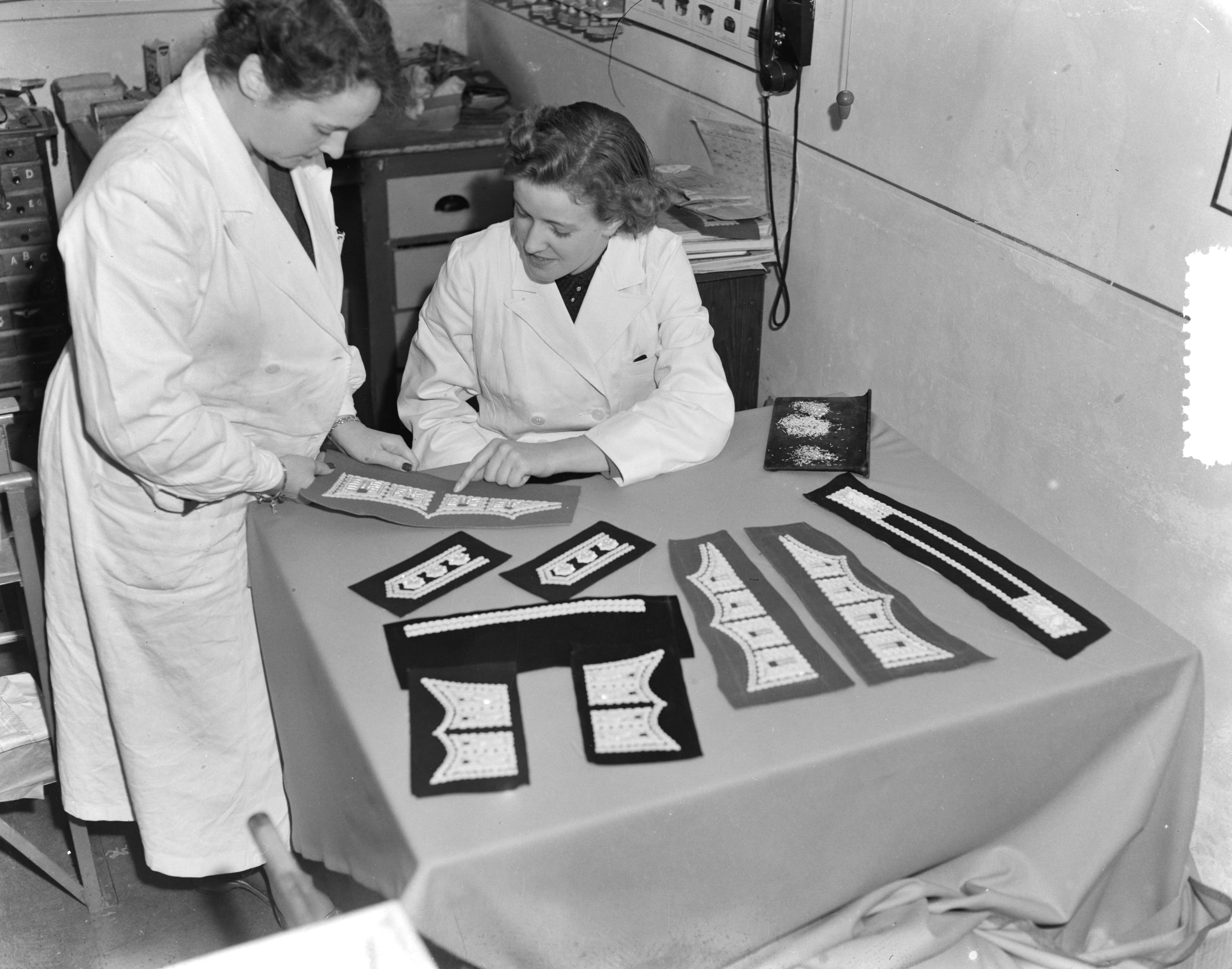 Fotocollectie Anefo — Bredase meisjes werken in Breda aan Engelse koningskleding. Het vervaardigen van borduursels voor de manchetsluitstukken voor de Welsh Guards — Foto: Duinen, G.W. van / Anefo. Licentie: Set B: Rechtenvrij / Publiek Domein. Bron: Nationaal Archief. http://hdl.handle.net/10648/a9054e14-d0b4-102d-bcf8-003048976d84