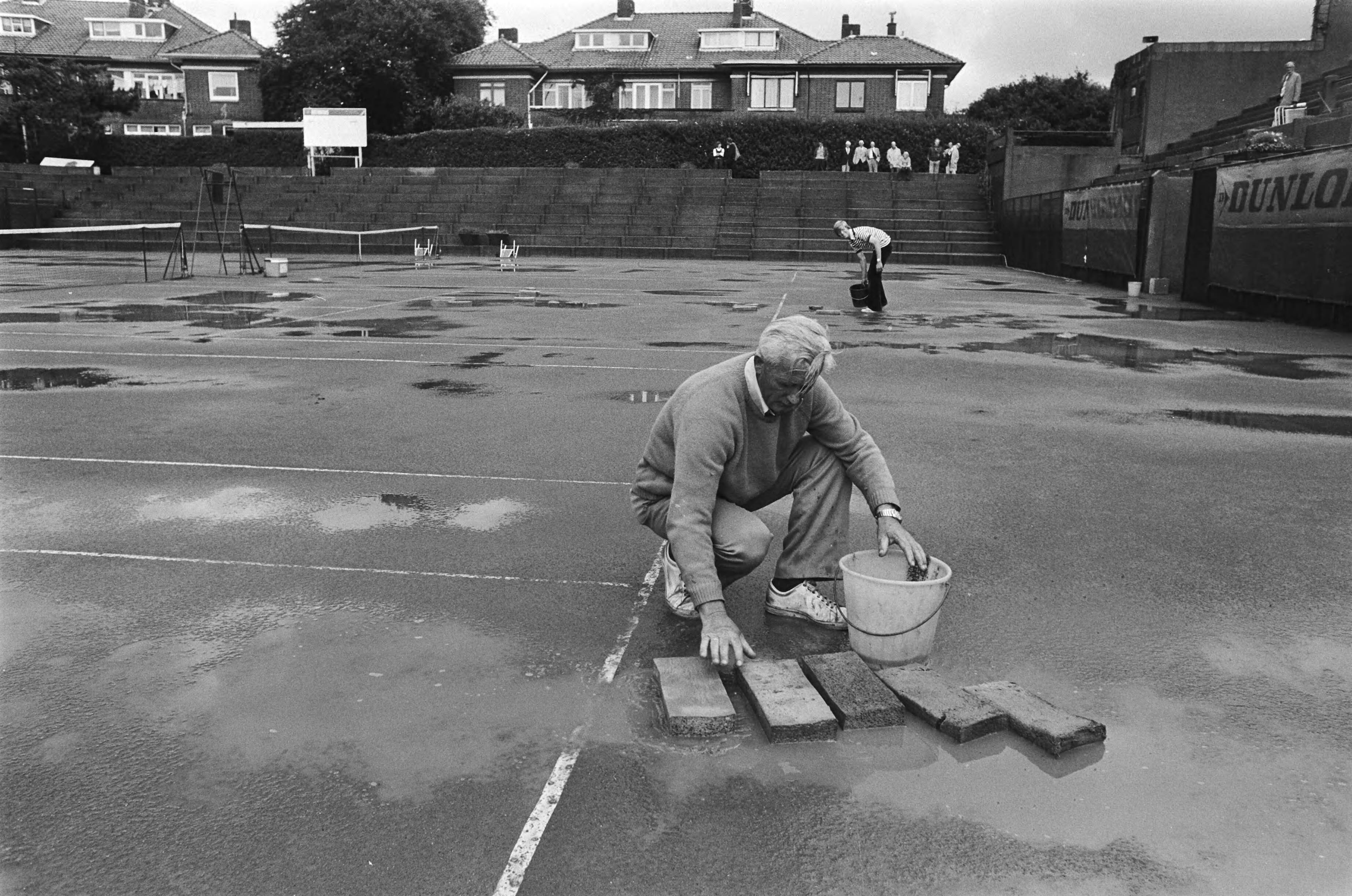 Fotocollectie Anefo — Nationale tenniskampioenschappen op METS, Den Haag ; plassen worden met sponzen te lijf gegaan — Foto: Verhoeff, Bert / Anefo. Licentie: Set B: Rechtenvrij / Publiek Domein. Bron: Nationaal Archief. http://hdl.handle.net/10648/acb9c15c-d0b4-102d-bcf8-003048976d84