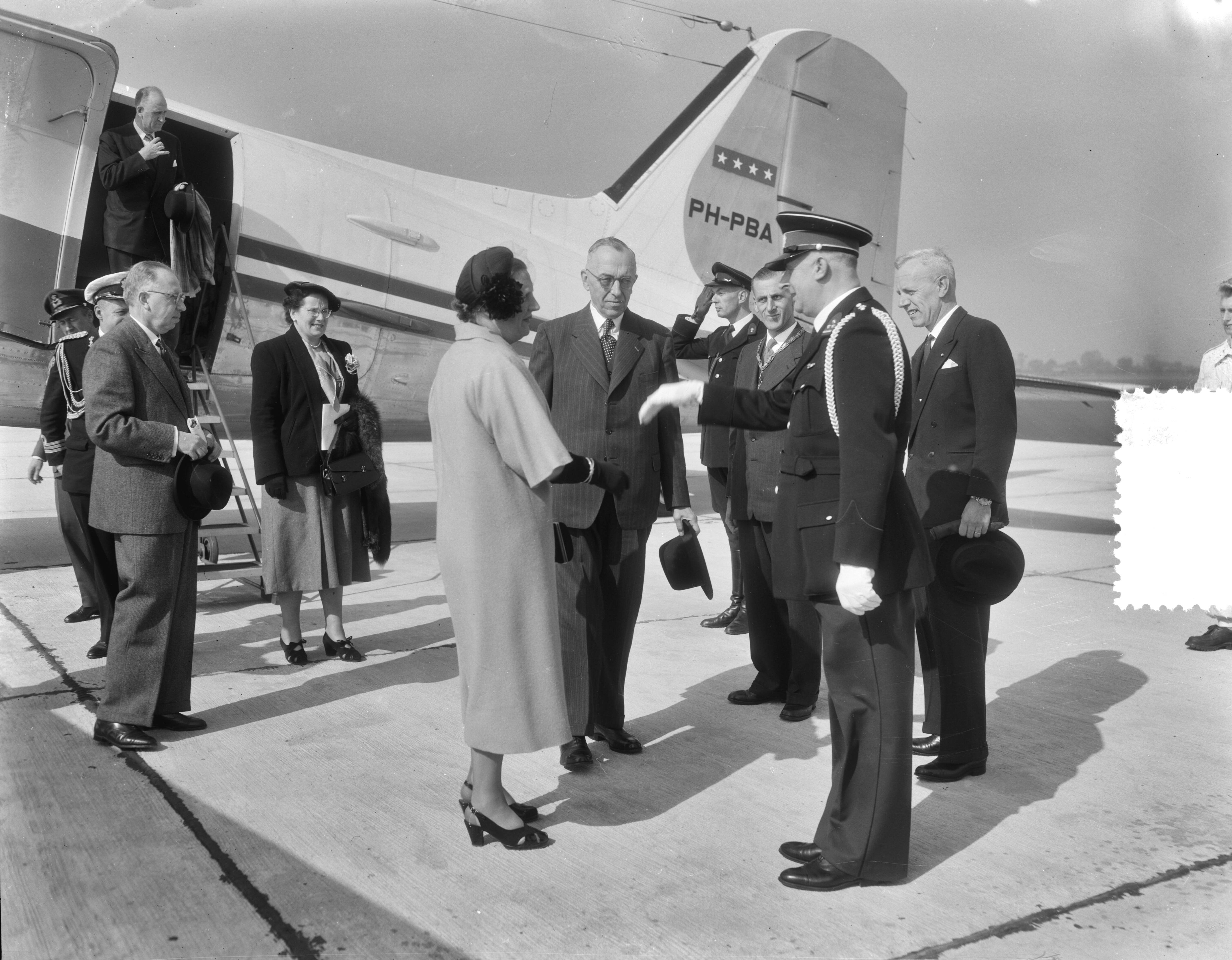 Werkbezoek van koningin Juliana aan de provincie Groningen (1954) — Werkbezoek van koningin Juliana aan de provincie Groningen. Aankomst op het vliegveld Eelde. Zij was in gezelschap van haar particulier secretaresse mevr. N. Smitt-Avis en haar adjudant, kapitein-luitenant-ter-zee J.G. Stegeman. Zij werd begroet door de Commissaris der Koningin in de provincie Groningen, dr. E.H. Ebels, de griffier van de Staten van Groningen, drs. J. Hangebroek, de burgemeester van Eelde, mr. B. Struben en andere autoriteiten — Foto: Duinen, G.W. van / Anefo. Licentie: Set B: Rechtenvrij / Publiek Domein. Bron: Nationaal Archief. http://hdl.handle.net/10648/a9228ef2-d0b4-102d-bcf8-003048976d84