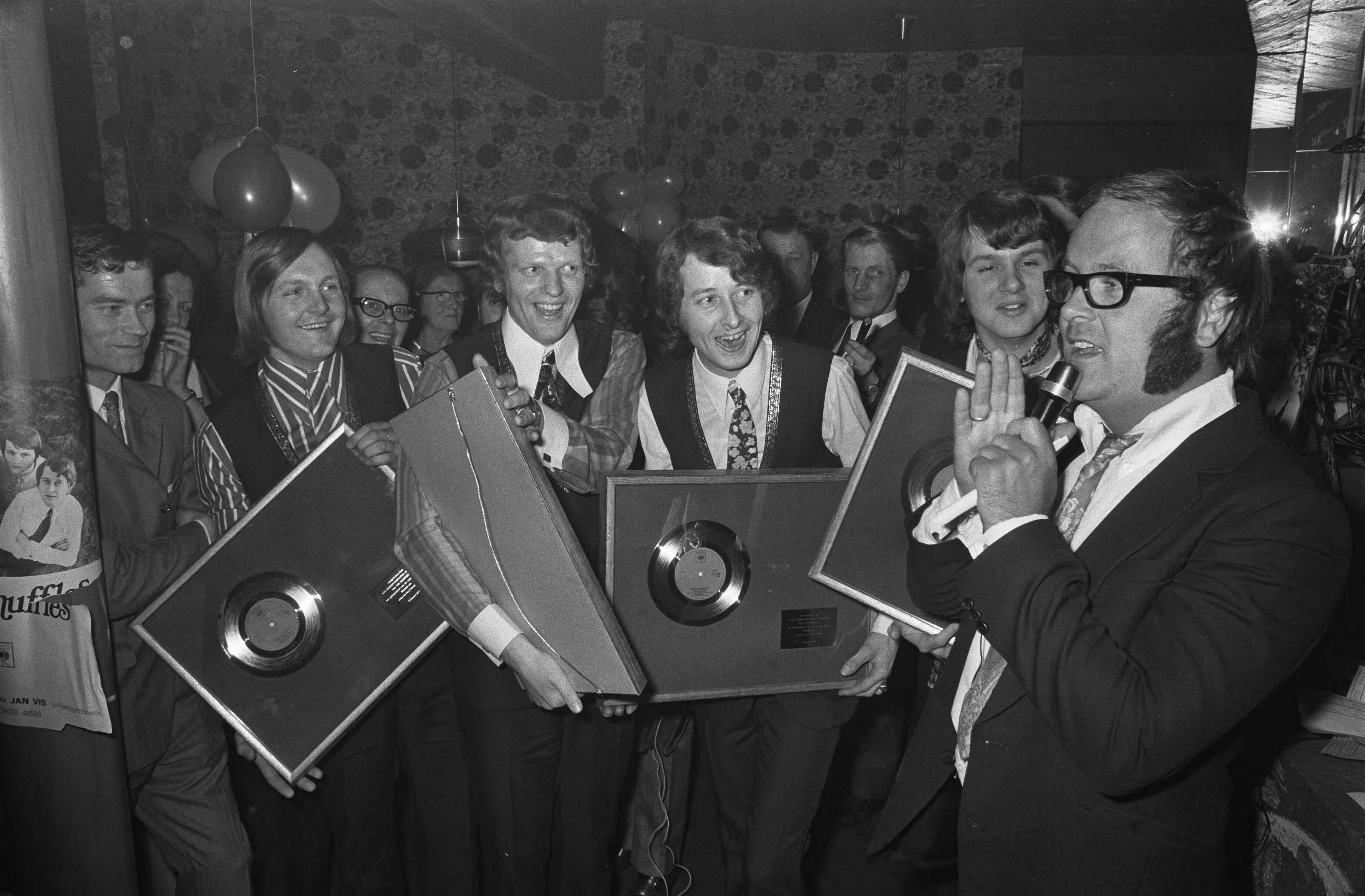 Fotocollectie Anefo — Popgroep The Shuffles ontvangt gouden plaat voor "Cha la la, I need you" in hotel Gooiland te Hilversum. The Shuffles met plaat, rechts Joost den Draaier (pseudoniem voor Willem van Kooten) — Foto: Verhoeff, Bert / Anefo. Licentie: Set B: Rechtenvrij / Publiek Domein. Bron: Nationaal Archief. http://hdl.handle.net/10648/ab8d24e0-d0b4-102d-bcf8-003048976d84
