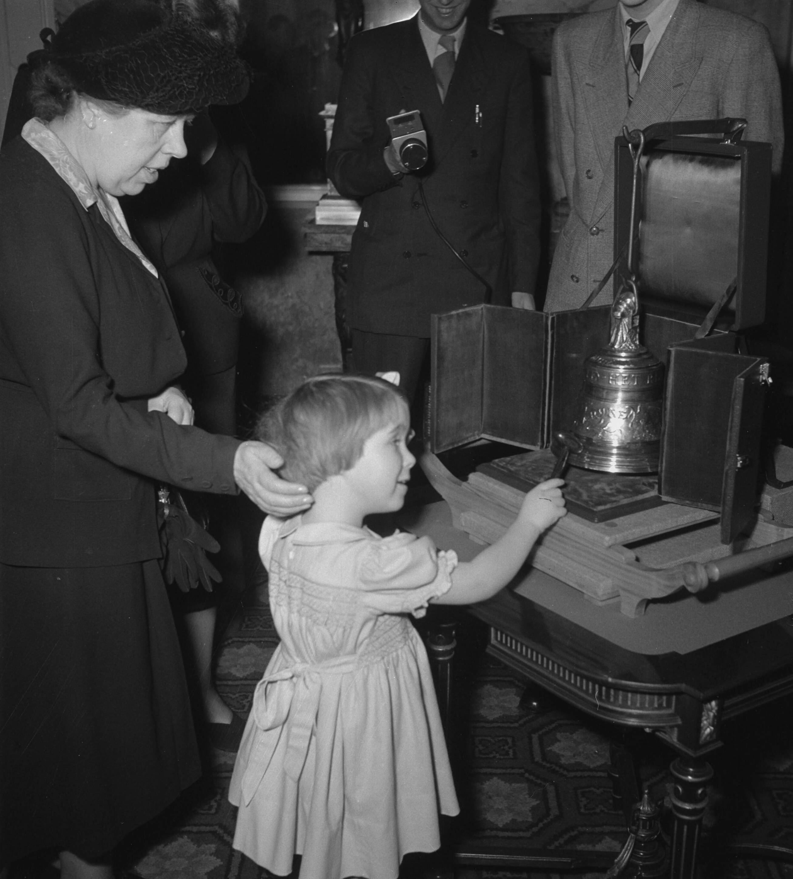Aanbieding op paleis Soestdijk aan prinses Christina van de kleinste luidklok, het z.g. Marijke-klokje, behorend tot het carillon dat Nederland als dank aan de Verenigde Staten zal geven — Prinses Marijke (Christina) slaat tegen het klokje; links freule Wttewaal van Stoetwegen — Foto: Noske, J.D. / Anefo. Licentie: Set B: Rechtenvrij / Publiek Domein. Bron: Nationaal Archief. http://hdl.handle.net/10648/a8f598f2-d0b4-102d-bcf8-003048976d84