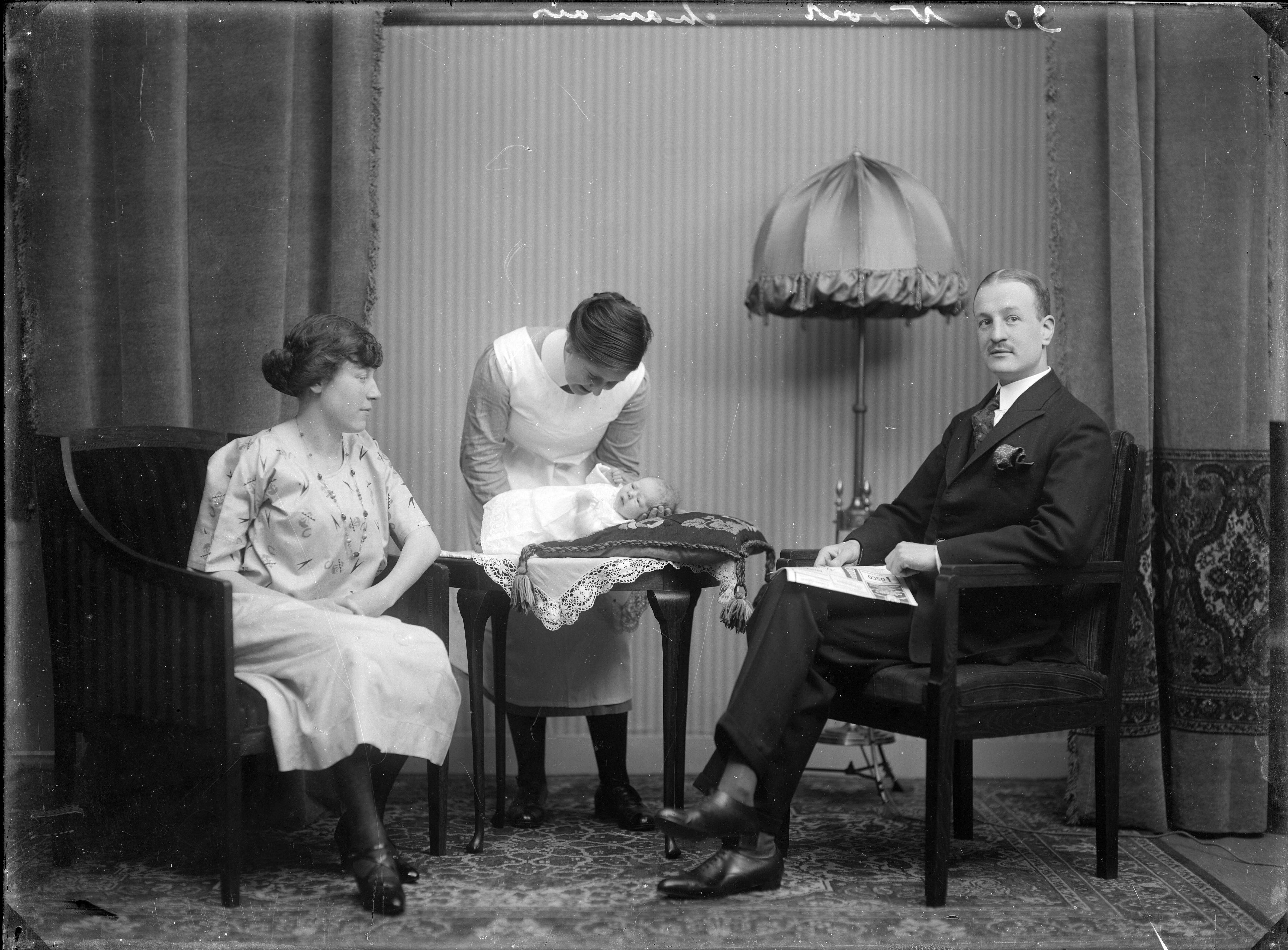 Berg, van den (BERG 050) — Echtparen. Huiskamer tafereel van een echtpaar met een kraamverzorgster in uniform en een baby liggend op een tafeltje met smyrna-kussen. Nederland. 1918-1930.30 Noort chamois — Foto: Berg, Th.C.J. van den / Spaarnestad Photo (05887). Licentie: Set B: Rechtenvrij / Publiek Domein. Bron: Nationaal Archief. http://hdl.handle.net/10648/35429da7-c5c3-a382-e063-6df0900a6686