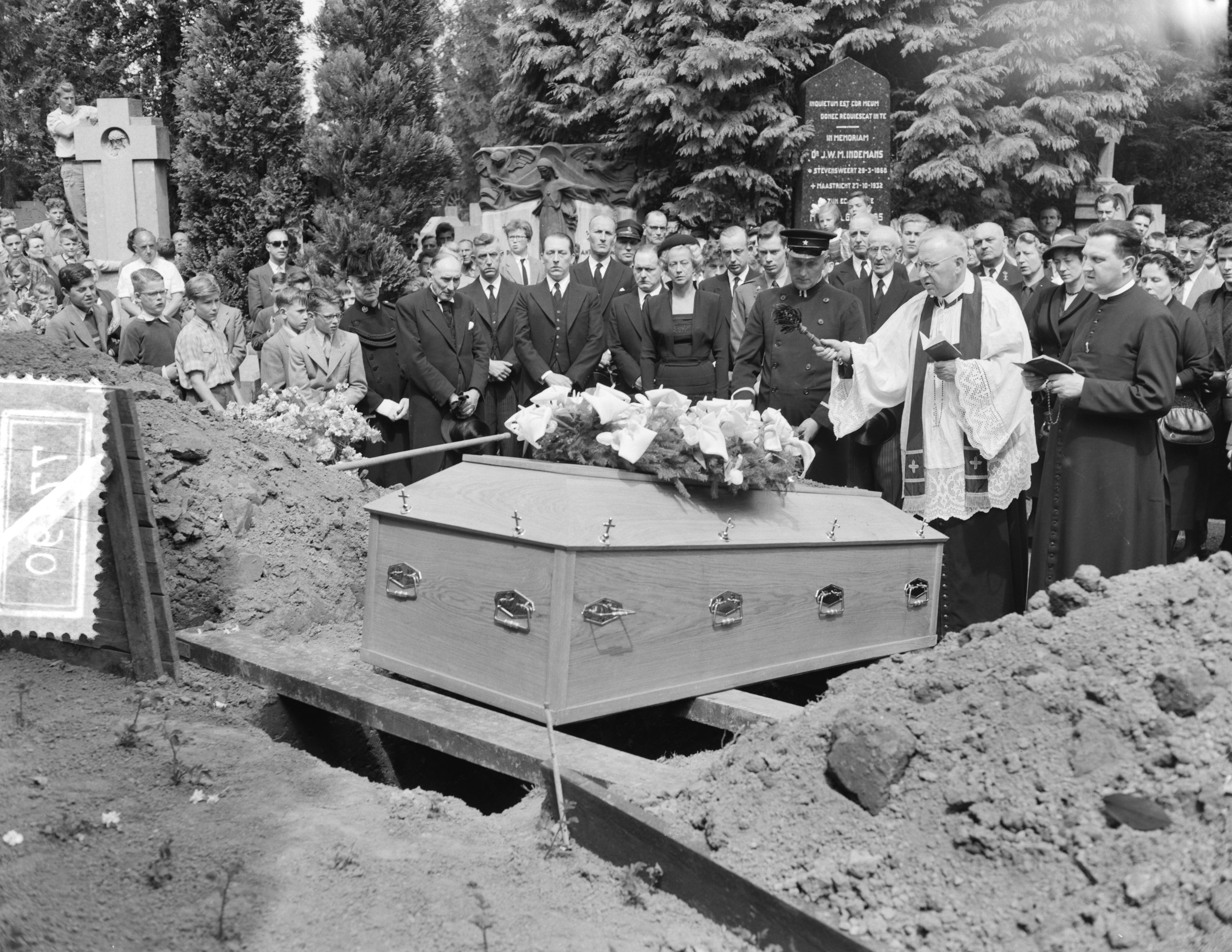 Fotocollectie Anefo — Begrafenis van Leon Jungschläger te Maastricht. Pastoor-deken van Maastricht P.J.M. Jennekens met wijwaterkwast. In het midden de weduwe Germaine Geuskens-Jungschläger — Foto: Rossem, Wim van / Anefo. Licentie: Set B: Rechtenvrij / Publiek Domein. Bron: Nationaal Archief. http://hdl.handle.net/10648/a947a1b0-d0b4-102d-bcf8-003048976d84