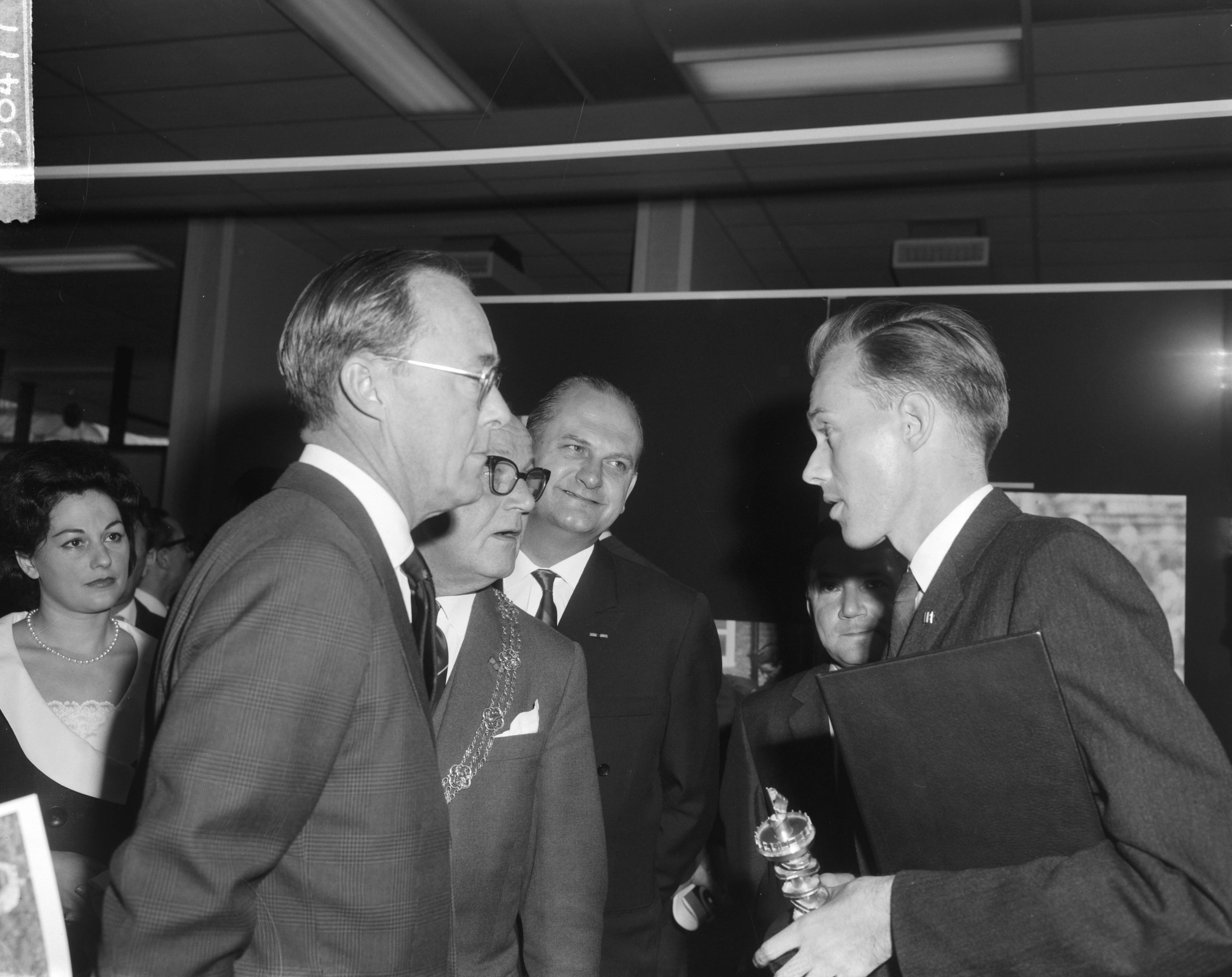 Fotocollectie Anefo — Prins Bernhard opende tentoonstelling World Press Photo 1963 in het Gemeentemuseum te Den Haag. De prins in gesprek met de winnaar van de hoofdprijs Malcolm W. Brown. Naast de prins (met ambtsketen) de burgemeester van Den Haag, mr. H.A.M.T. Kolfschoten — Foto: Bilsen, Joop van / Anefo. Licentie: Set B: Rechtenvrij / Publiek Domein. Bron: Nationaal Archief. http://hdl.handle.net/10648/aa51ffba-d0b4-102d-bcf8-003048976d84