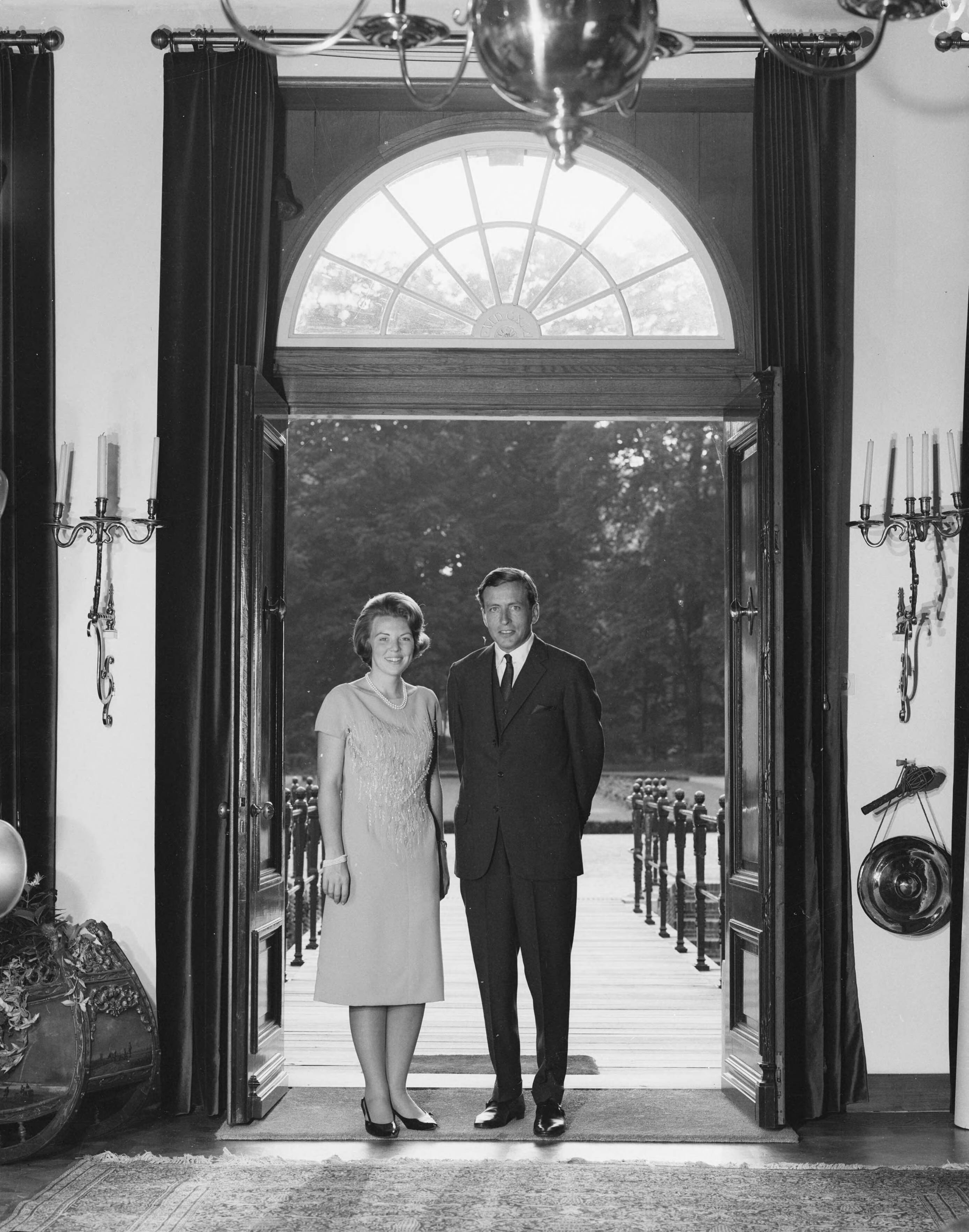 Fotocollectie RVD / Koninklijk Huis — Prinses Beatrix en Claus von Amsberg in de deuropening van kasteel Drakensteyn, enkele dagen voordat hun verloving op 28 juni 1965 officieel wordt aangekondigd — Foto: Koot, Max / RVD. Licentie: Set B: Rechtenvrij / Publiek Domein. Bron: Nationaal Archief. http://hdl.handle.net/10648/afbbbf22-d0b4-102d-bcf8-003048976d84