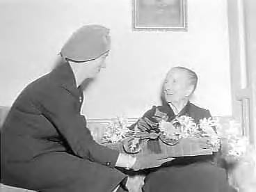 Fotocollectie Anefo — Oudste inwoonster van Den Haag, mevrouw J.J. de Calonne-Meister wordt 108 jaar en wordt gefeliciteerd door mevr. Kolfschoten, de echtgenote van de burgemeester van Den Haag — Foto: Pot, Harry / Anefo. Licentie: Set B: Rechtenvrij / Publiek Domein. Bron: Nationaal Archief. http://hdl.handle.net/10648/a96e4db0-d0b4-102d-bcf8-003048976d84