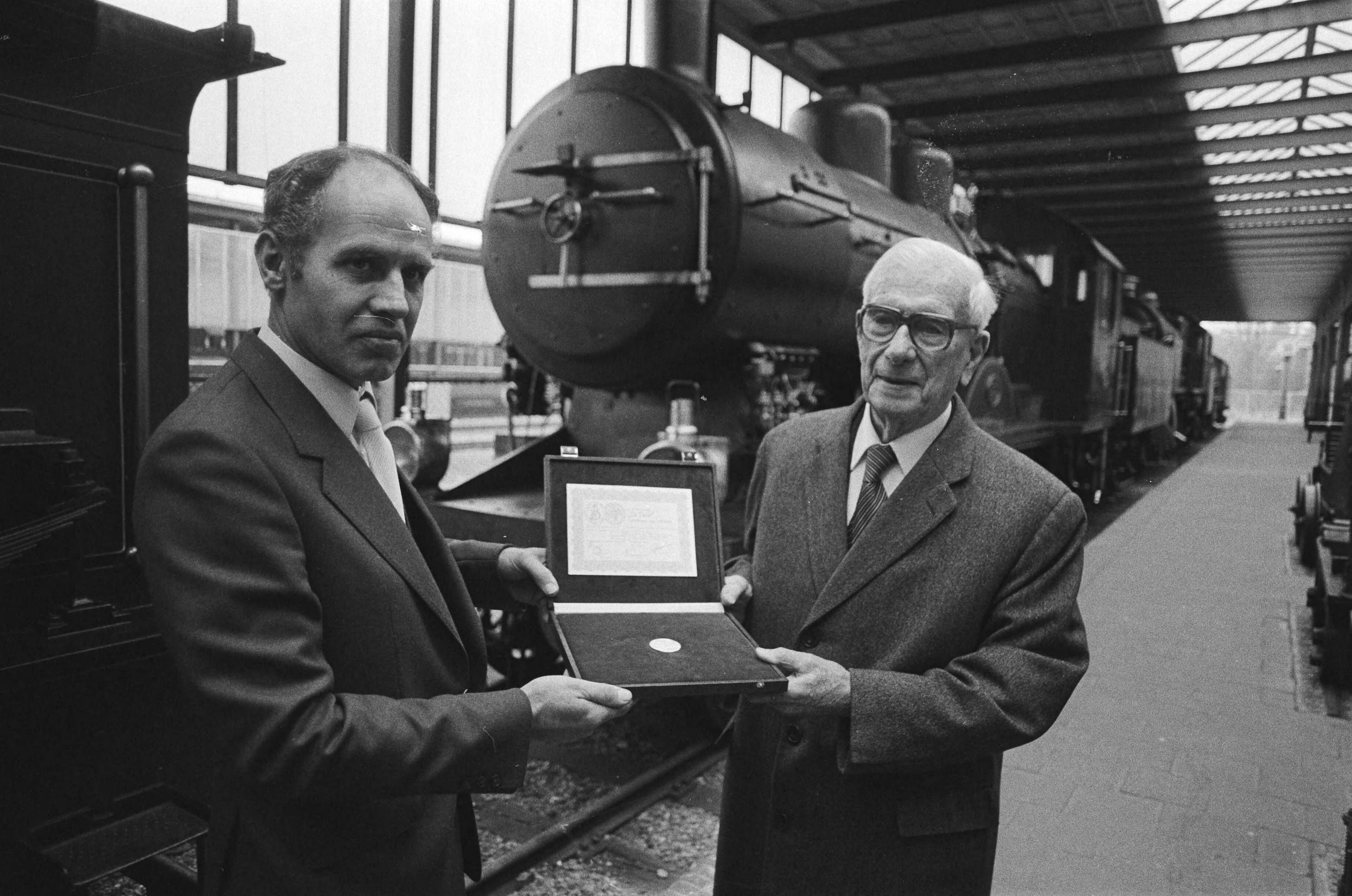 Fotocollectie Anefo — Dr. ir. F. Q. Den Hollander (oud-president NS) (r.) krijgt in het Spoorwegmuseum in Utrecht 1ste exemplaar serie US-herdenkingsmunten door E. M. Meupelerberg / — Foto: Antonisse, Marcel / Anefo. Licentie: Set B: Rechtenvrij / Publiek Domein. Bron: Nationaal Archief. http://hdl.handle.net/10648/ad102358-d0b4-102d-bcf8-003048976d84