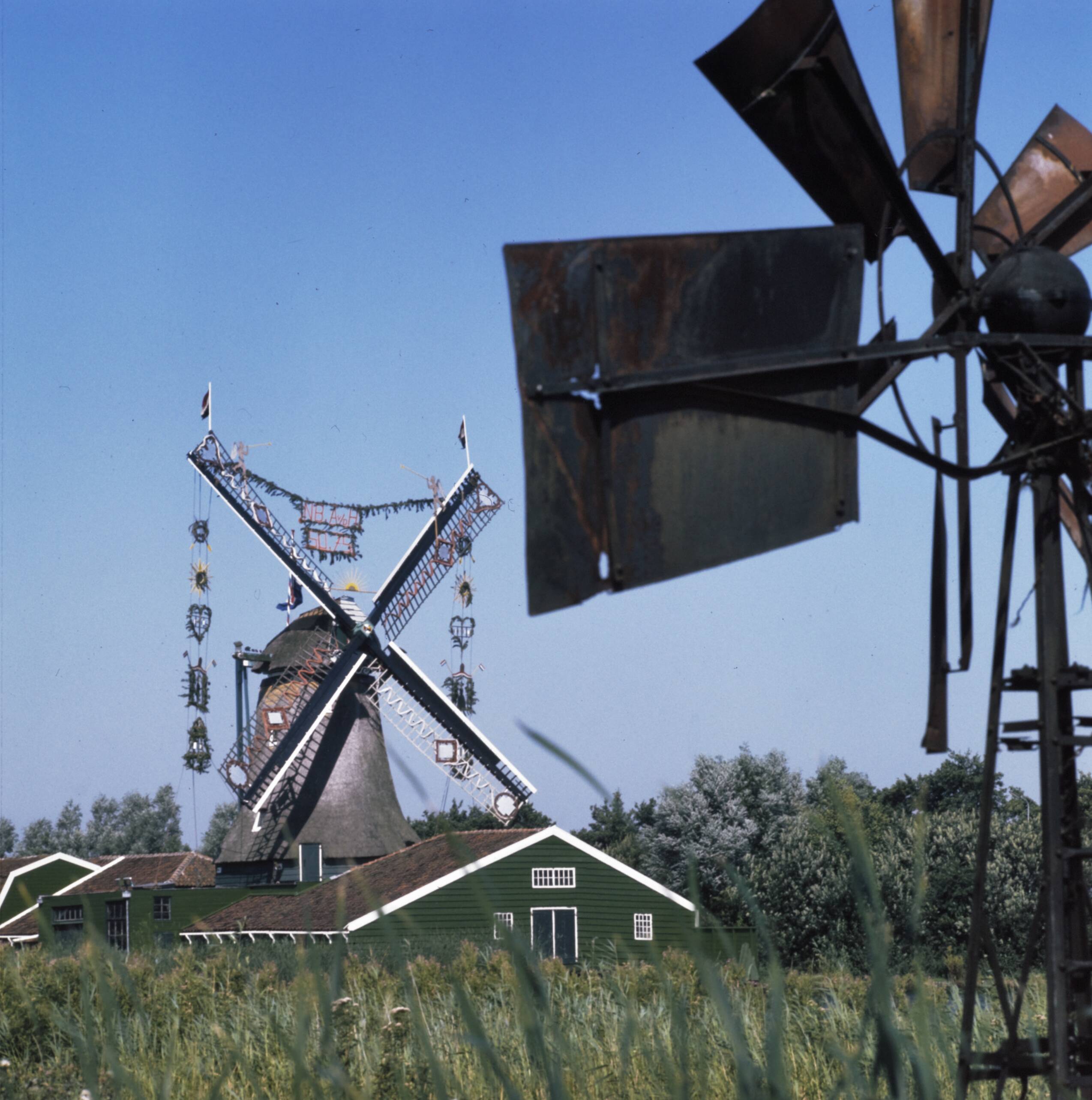 Fotocollectie Anefo — Zaanse Schans molens. Meisjes. Papiermolen De Schoolmeester te Westzaan, in feesttooi, 6-kante stellingmolen, bouwjaar 1692 — Foto: Mieremet, Rob / Anefo. Licentie: Set B: Rechtenvrij / Publiek Domein. Bron: Nationaal Archief. http://hdl.handle.net/10648/ad93afb6-d0b4-102d-bcf8-003048976d84