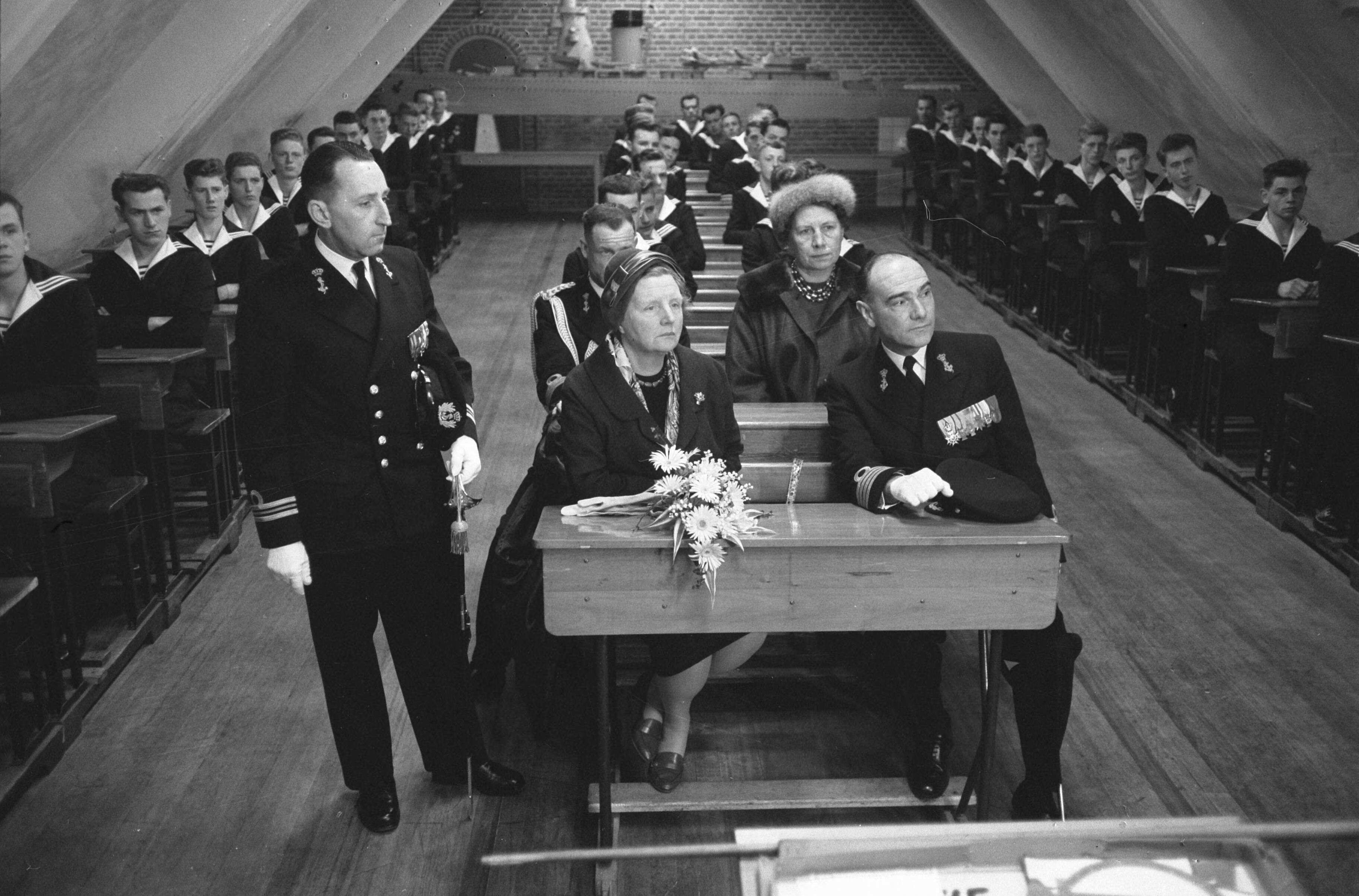 Fotocollectie Anefo — Koningin Juliana bezoekt marinekamp Loosdrecht. De koningin volgt een les over het verkeer in een schoolbank met naast haar de commandant van het opleidingscentrum kapitein-ter-zee H.J. Baay — Foto: Pot, Harry / Anefo. Licentie: Set B: Rechtenvrij / Publiek Domein. Bron: Nationaal Archief. http://hdl.handle.net/10648/a9ce32b6-d0b4-102d-bcf8-003048976d84