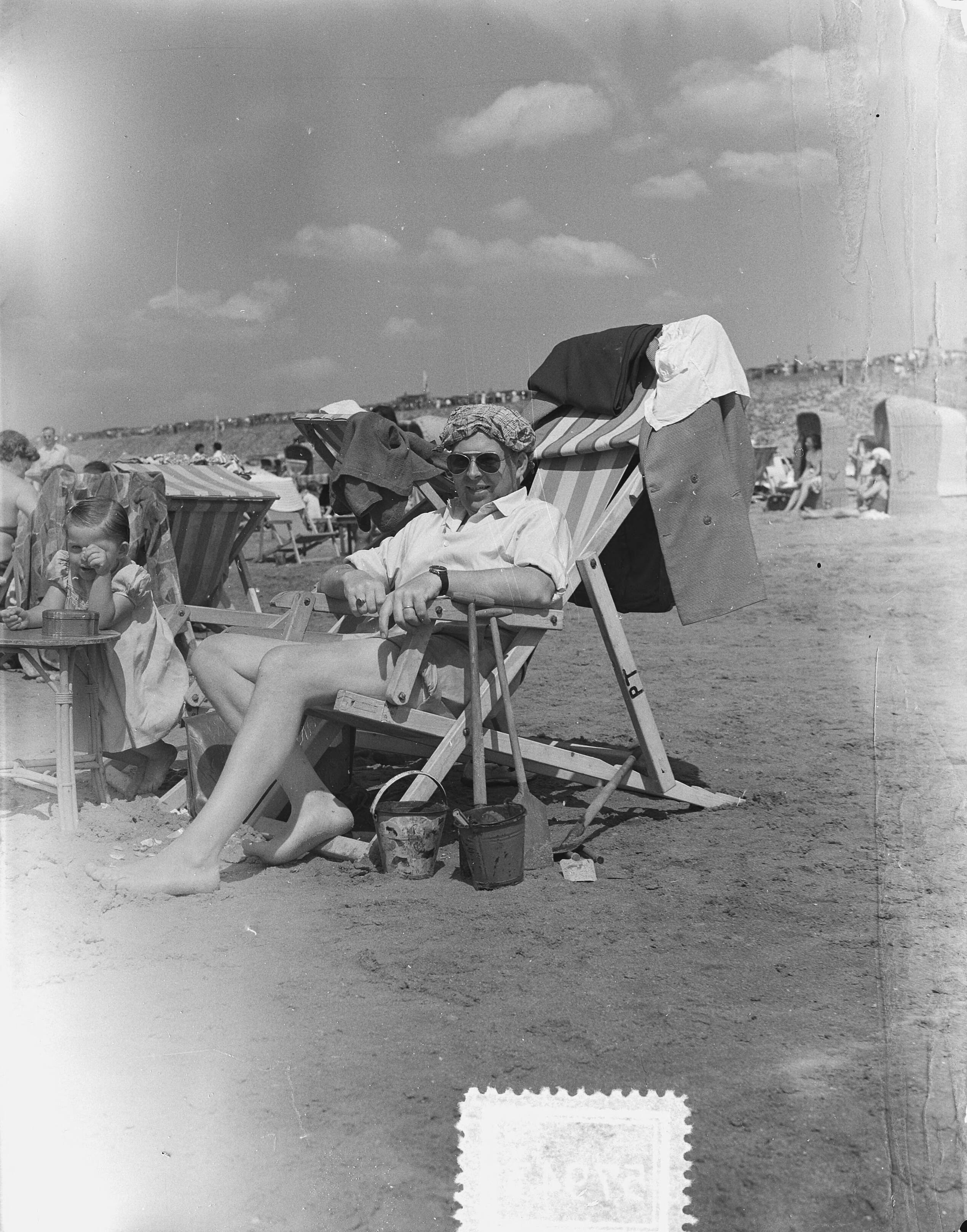 Fotocollectie Anefo — Zomerplaatjes. Drukte op het strand van Zandvoort. Man in strandstoel met bedekte schedel — Foto: Rossem, Wim van / Anefo. Licentie: Set B: Rechtenvrij / Publiek Domein. Bron: Nationaal Archief. http://hdl.handle.net/10648/a90e339e-d0b4-102d-bcf8-003048976d84