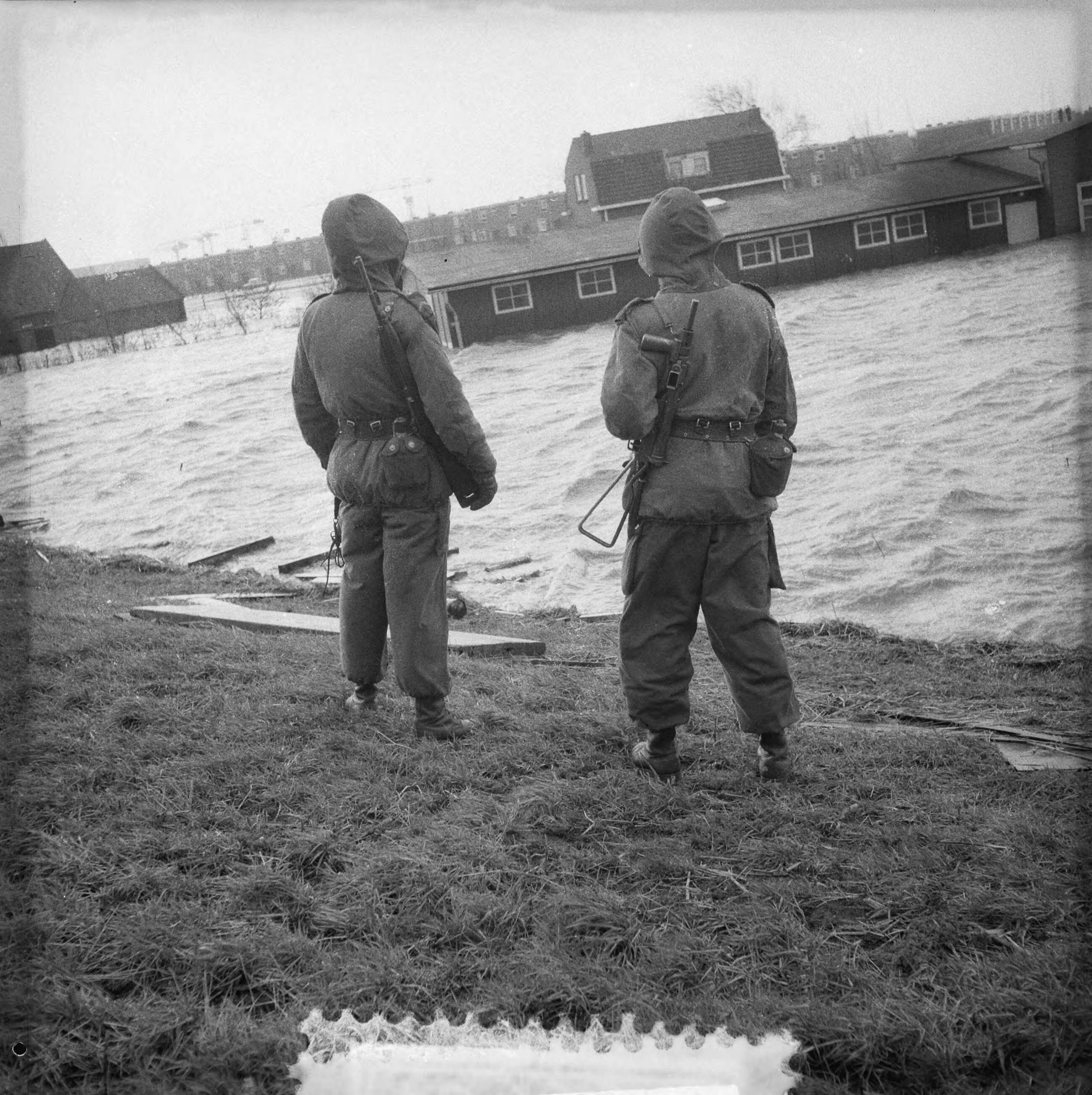 Ramp Tuindorp Oostzaan — Ramp Tuindorp Oostzaan [twee gewapende militairen staan op een dijk en kijken naar het overstromingsgebied] — Foto: Lindeboom, Henk / Anefo. Licentie: Set B: Rechtenvrij / Publiek Domein. Bron: Nationaal Archief. http://hdl.handle.net/10648/a9a62d16-d0b4-102d-bcf8-003048976d84