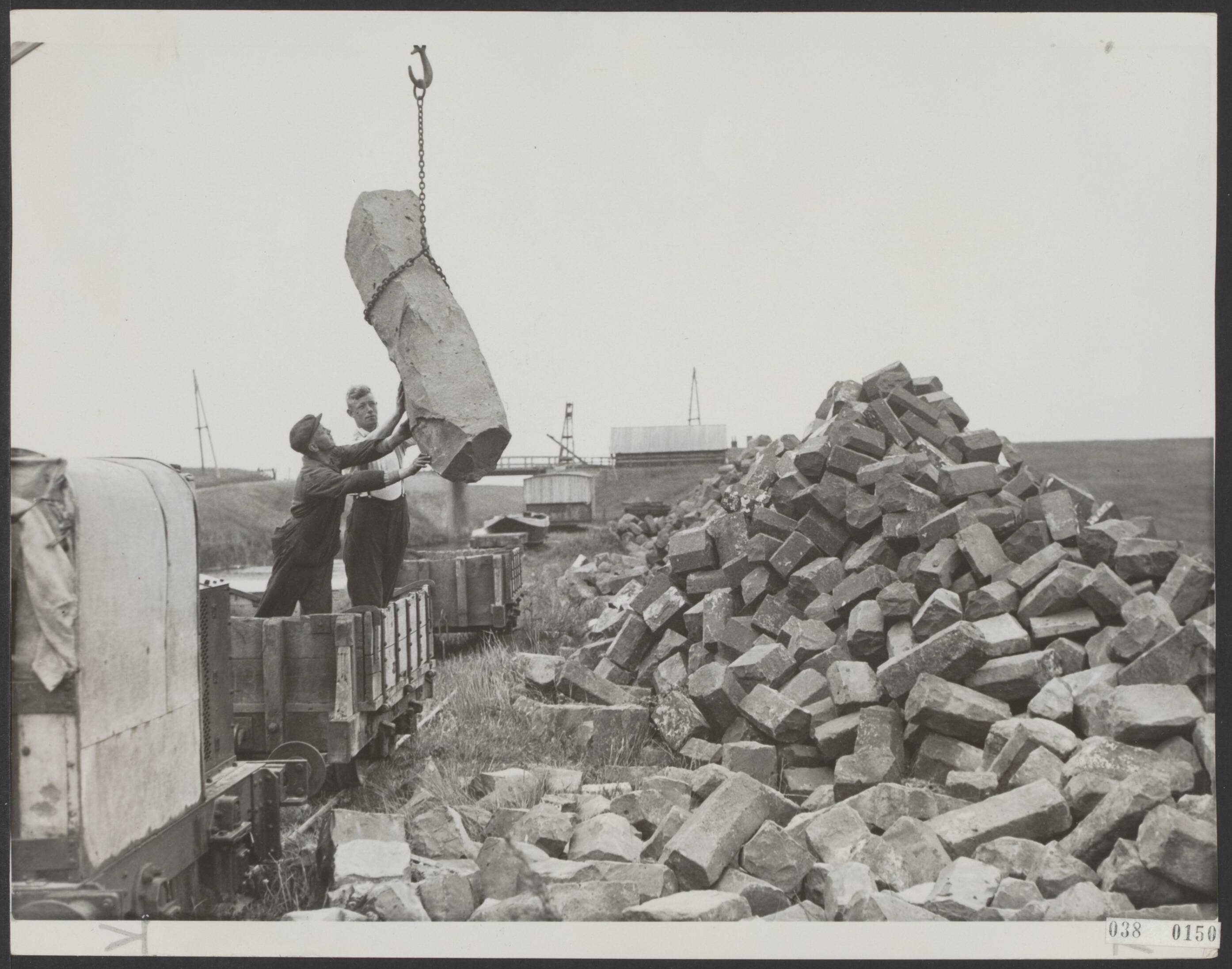 Fotocollectie Elsevier Binnenland — Begin van de herstelling, op grote schaal, van de Hondsbossche Zeewering. De strekdammen zullen geheel worden vernieuwd, terwijl de dijk opgehoogd zal worden. Enorme grote stukken basaltblokken worden vervoerd naar de zeekant — Foto: N.V. Polygoon. Licentie: Set B: Rechtenvrij / Publiek Domein. Bron: Nationaal Archief. http://hdl.handle.net/10648/adf0d178-d0b4-102d-bcf8-003048976d84