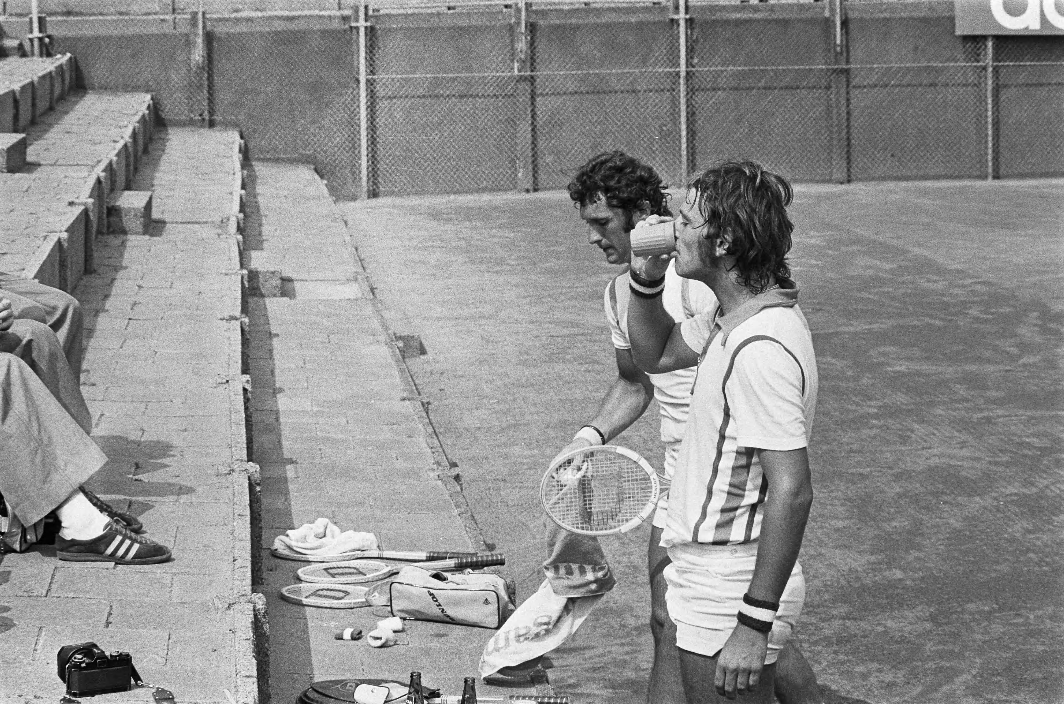 Nationale tenniskampioenschappen op de METS-tennisbanen 1975 — Hordijk (l) en Koning pauzeren tijdens hun wedstrijd — Foto: Mieremet, Rob / Anefo. Licentie: Set B: Rechtenvrij / Publiek Domein. Bron: Nationaal Archief. http://hdl.handle.net/10648/ac6f9b36-d0b4-102d-bcf8-003048976d84