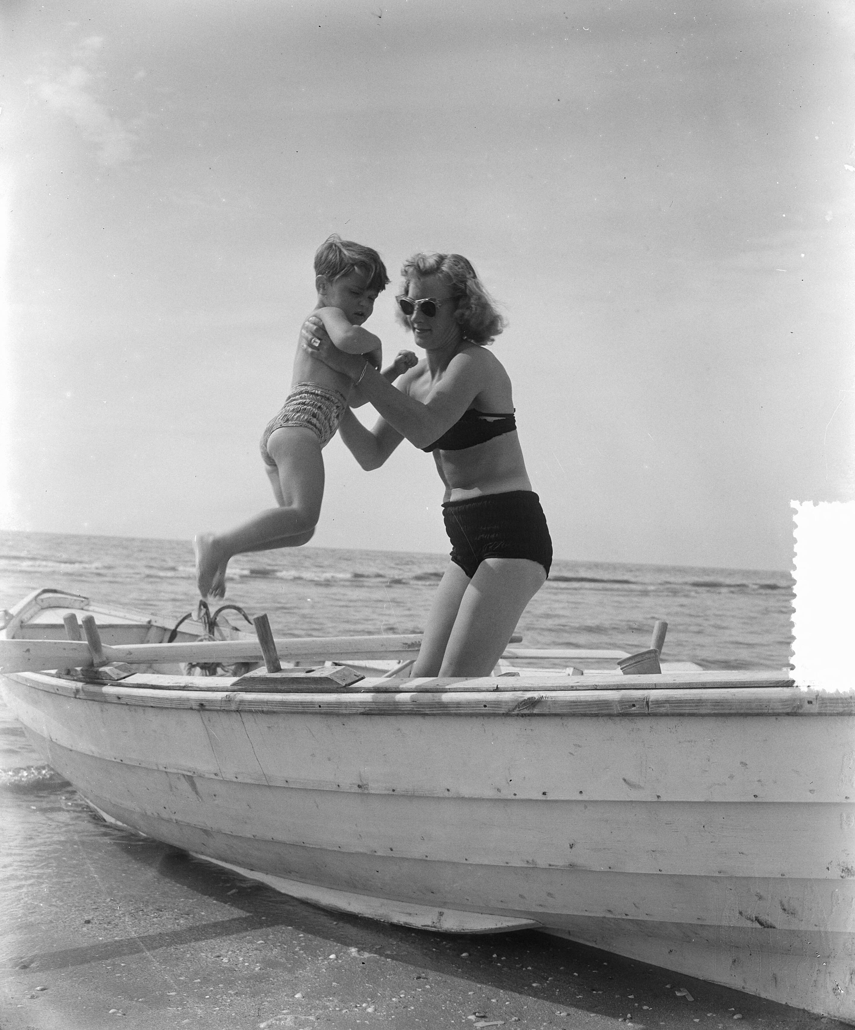 Fotocollectie Anefo — Zomerplaatjes aan strand van Zandvoort. Moeder tilt kind in een roeiboot — Foto: Pot, Harry / Anefo. Licentie: Set B: Rechtenvrij / Publiek Domein. Bron: Nationaal Archief. http://hdl.handle.net/10648/a90e5586-d0b4-102d-bcf8-003048976d84