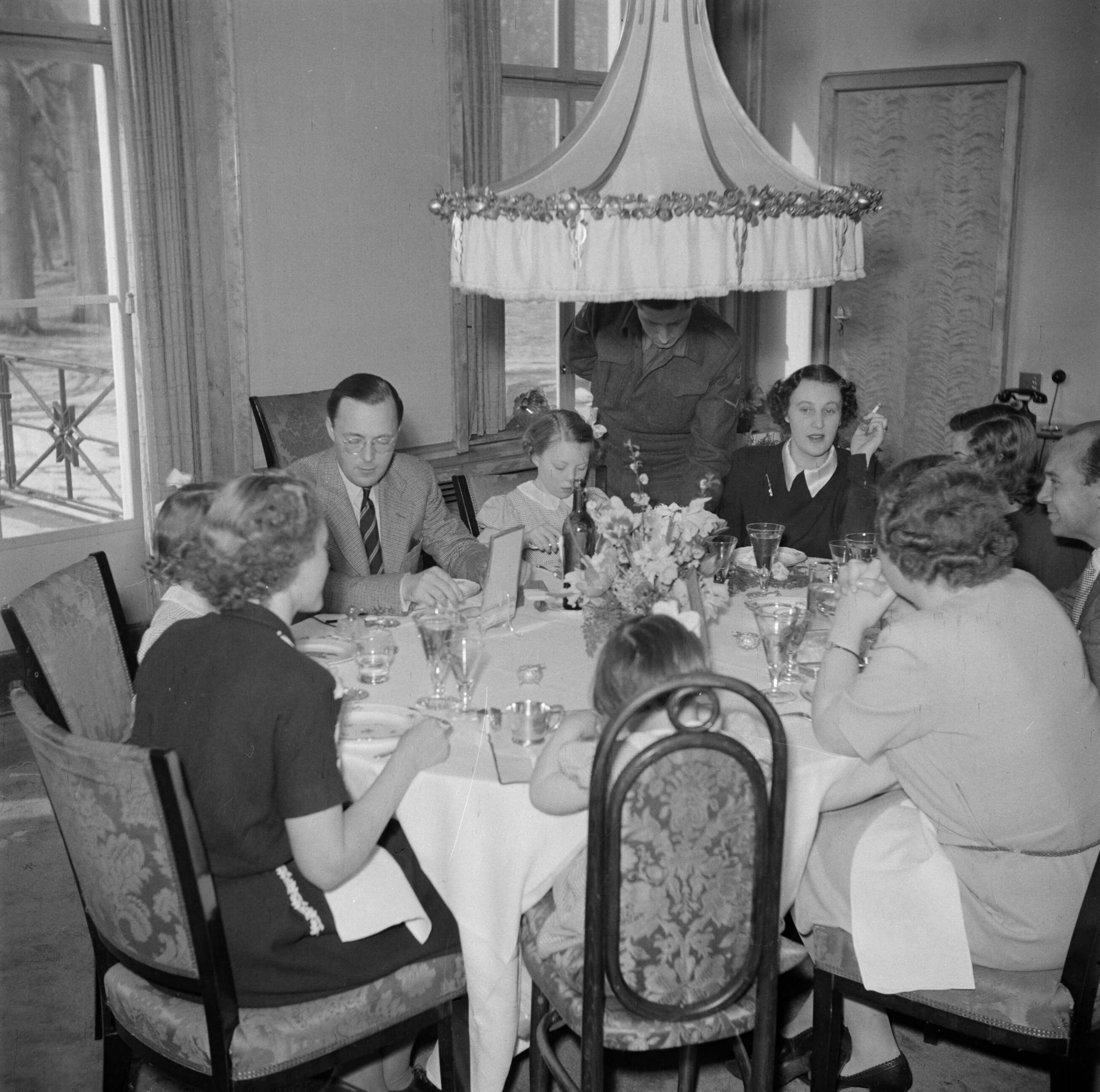 De koninklijke familie op Soestdijk — Prinses Juliana, prins Bernhard, hundochters en personeelsleden aan de eetttafel — Foto: Poll, Willem van de. Licentie: Set B: Rechtenvrij / Publiek Domein. Bron: Nationaal Archief. http://hdl.handle.net/10648/aee921d4-d0b4-102d-bcf8-003048976d84