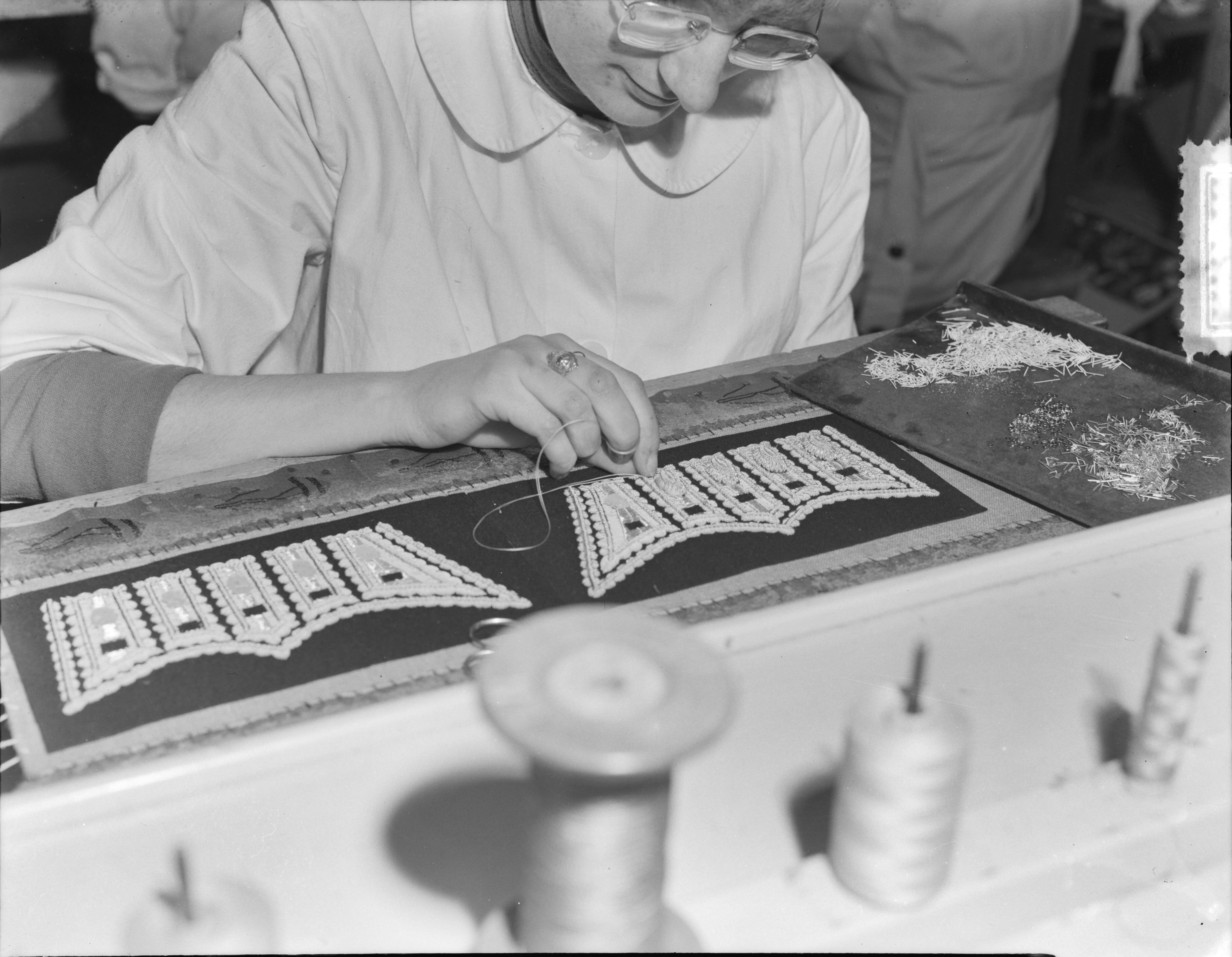 Fotocollectie Anefo — Bredase meisjes werken in Breda aan Engelse koningskleding. Het vervaardigen van borduursels voor de manchetsluitstukken voor de Welsh Guards — Foto: Duinen, G.W. van / Anefo. Licentie: Set B: Rechtenvrij / Publiek Domein. Bron: Nationaal Archief. http://hdl.handle.net/10648/a9054d56-d0b4-102d-bcf8-003048976d84