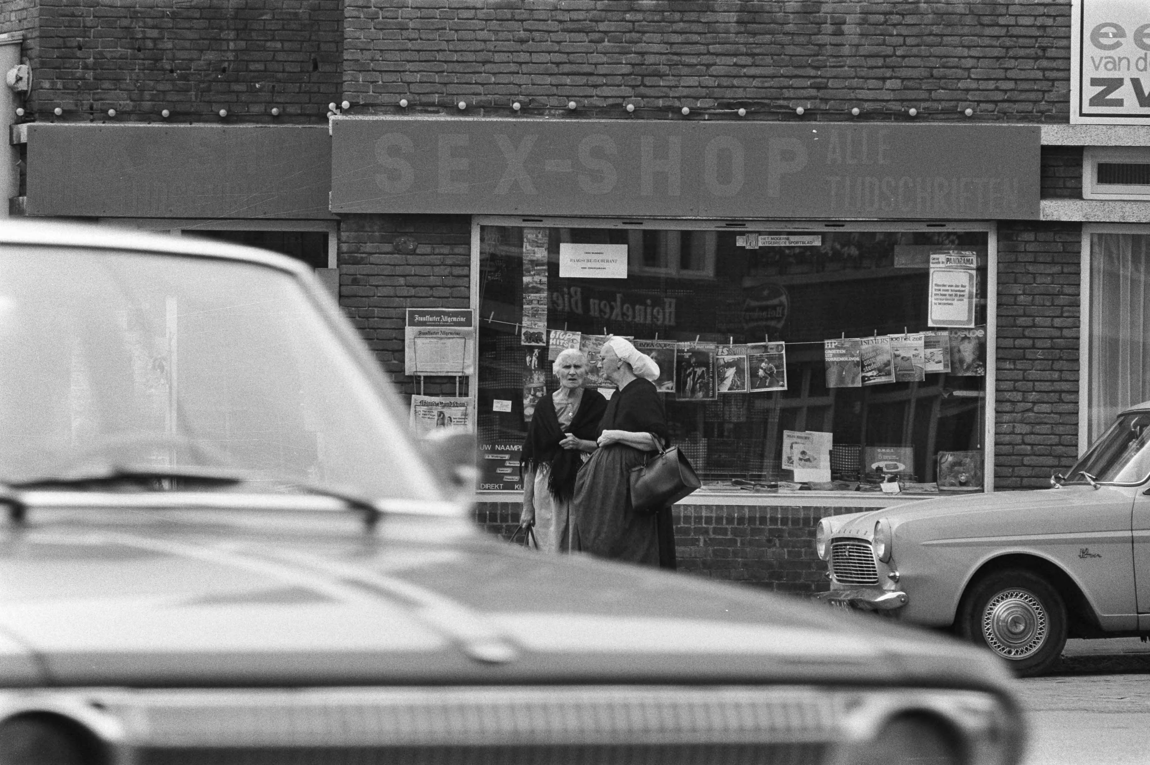 Fotocollectie Anefo — Vrouwen in klederdracht voor sexshop Scheveningen — Foto: Verhoeff, Bert / Anefo. Licentie: Set B: Rechtenvrij / Publiek Domein. Bron: Nationaal Archief. http://hdl.handle.net/10648/abc98d86-d0b4-102d-bcf8-003048976d84