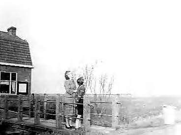Fotocollectie Anefo — Het dorp Rijk in de Haarlemmermeer zal verdwijnen voor startbaan Schiphol. Voor 1 maart 1959 moet het dorp verdwenen zijn. Mevrouw Overbeek met haar dochtertje kijken mistroostig naar de oorzaak van hun verhuizing — Foto: Pot, Harry / Anefo. Licentie: Set B: Rechtenvrij / Publiek Domein. Bron: Nationaal Archief. http://hdl.handle.net/10648/a95461ac-d0b4-102d-bcf8-003048976d84