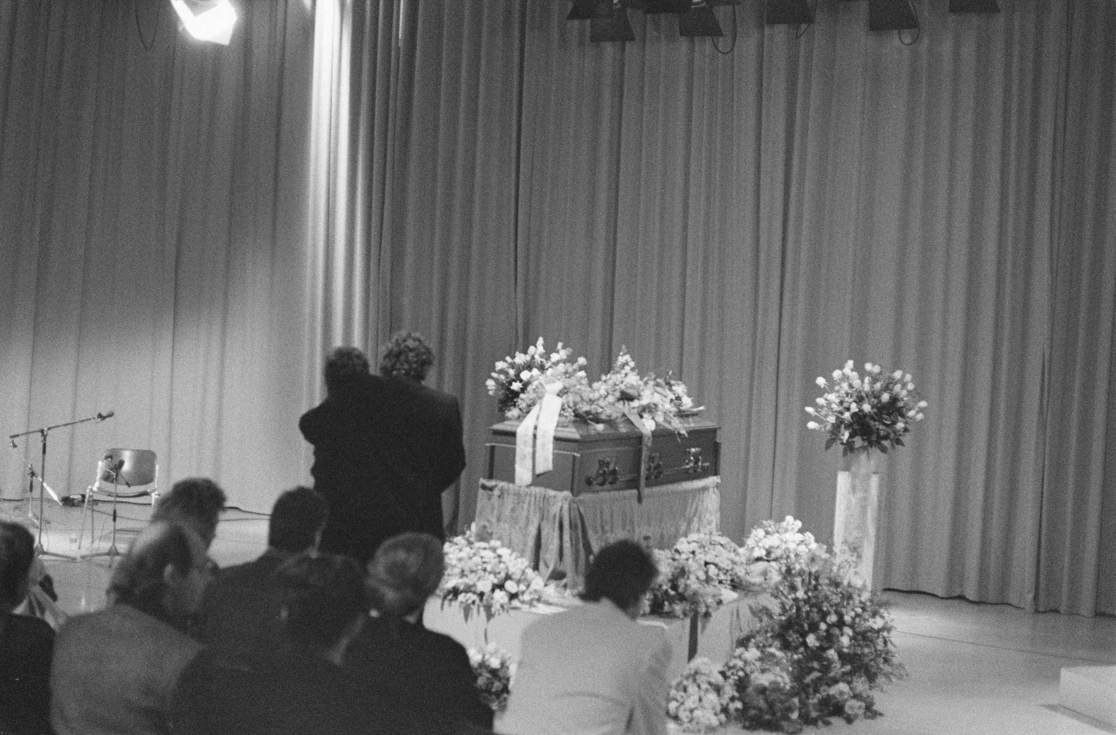 Herdenkingsdienst voor de doodgeschoten cameraman Cornel Lagrouw in Hilversum — Aanwezigen zitten in de ruimte waar de kist met bloemen staat — Foto: Bogaerts, Rob / Anefo. Licentie: Set B: Rechtenvrij / Publiek Domein. Bron: Nationaal Archief. http://hdl.handle.net/10648/ad71d5f8-d0b4-102d-bcf8-003048976d84