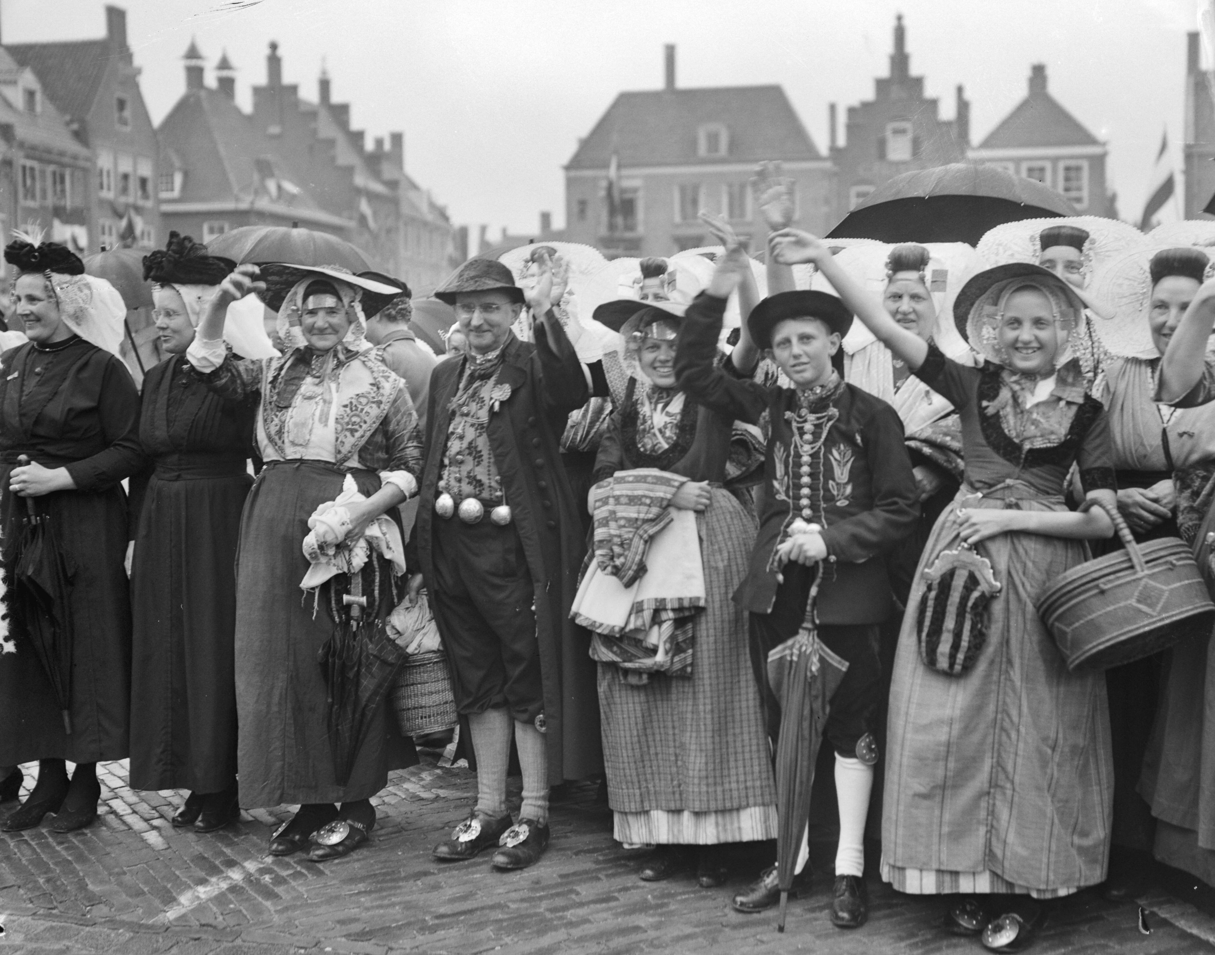 Koningin Juliana en prins Bernhard bezoeken Walcheren — Mannen en vrouwen in klederdracht wuiven naar het koninklijk paar — Foto: Bilsen, Joop van / Anefo. Licentie: Set B: Rechtenvrij / Publiek Domein. Bron: Nationaal Archief. http://hdl.handle.net/10648/a9245db8-d0b4-102d-bcf8-003048976d84