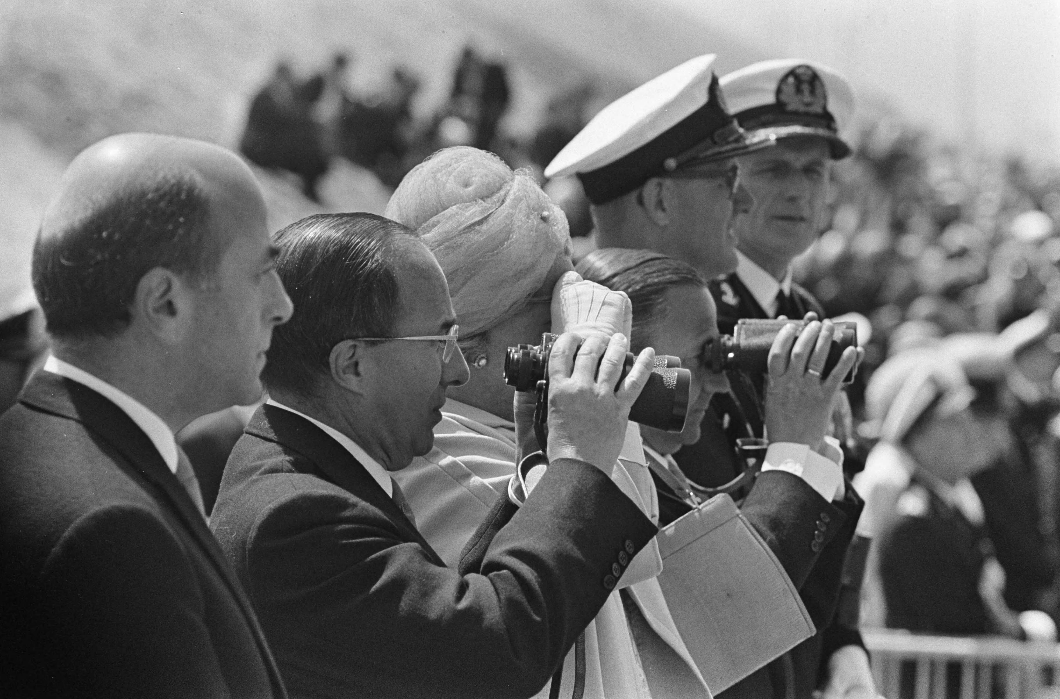 Koningin Juliana onthult het Marinemonument te Scheveningen — Met verrekijkers bestuderen de aanwezigen het defilé van alle marineonderdelen — Foto: Koch, Eric / Anefo. Licentie: Set B: Rechtenvrij / Publiek Domein. Bron: Nationaal Archief. http://hdl.handle.net/10648/aaee8448-d0b4-102d-bcf8-003048976d84