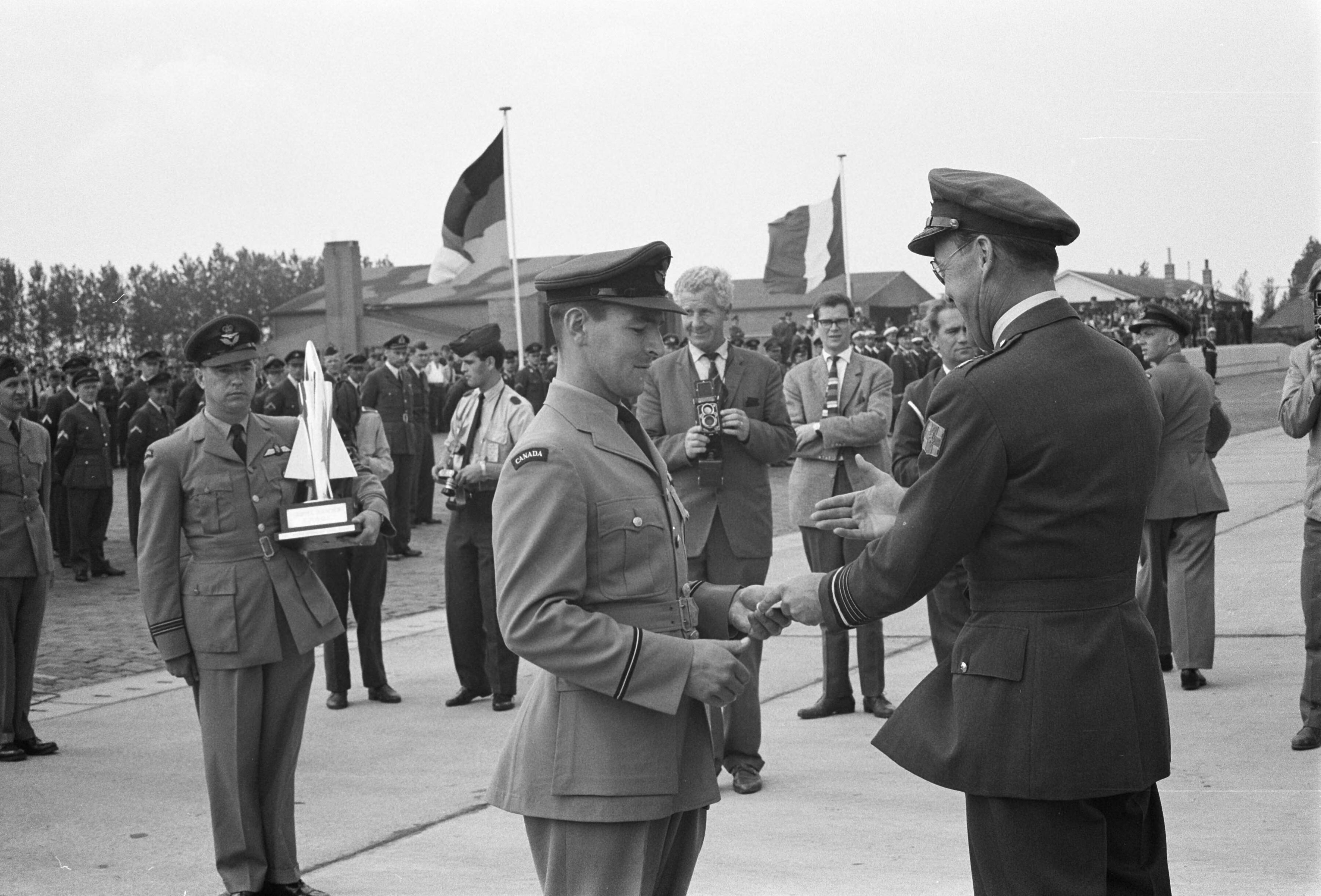 Fotocollectie Anefo — Prins Bernhard bij schietcompetitie NATO-Luchtmacht op vliegbasis Leeuwarden. De prins reikt een medaille uit aan een lid van het winnende Canadese team — Foto: Rossem, Wim van / Anefo. Licentie: Set B: Rechtenvrij / Publiek Domein. Bron: Nationaal Archief. http://hdl.handle.net/10648/a9dbe30c-d0b4-102d-bcf8-003048976d84