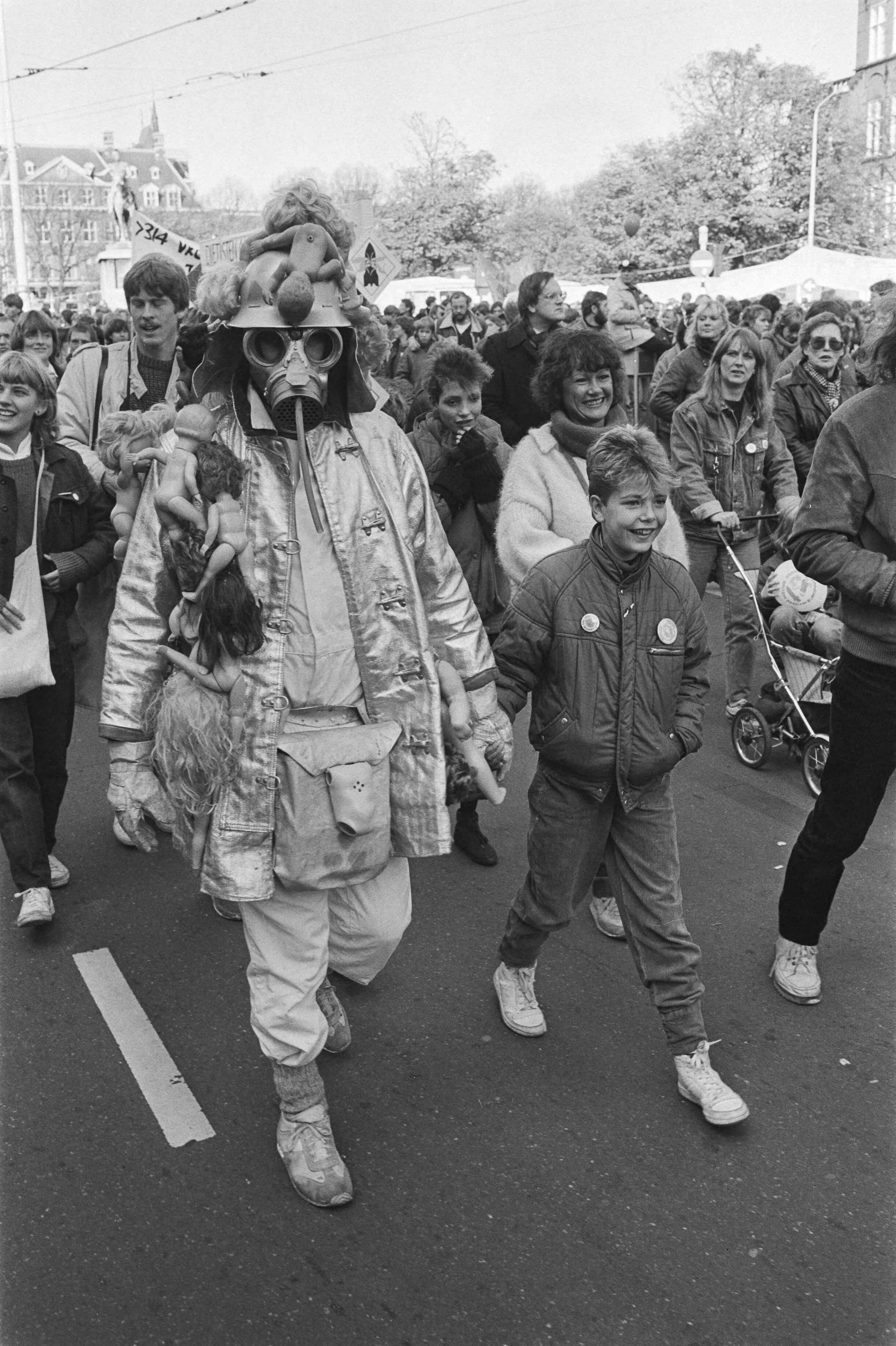 Vredesdemonstratie Den Haag , 550.000 mensen demonstreren o.m. tegen plaatsing kruisrakette — Demonstrant met gasmasker en helm behangen met poppen — Foto: Antonisse, Marcel / Anefo. Licentie: Set B: Rechtenvrij / Publiek Domein. Bron: Nationaal Archief. http://hdl.handle.net/10648/ad2fe256-d0b4-102d-bcf8-003048976d84