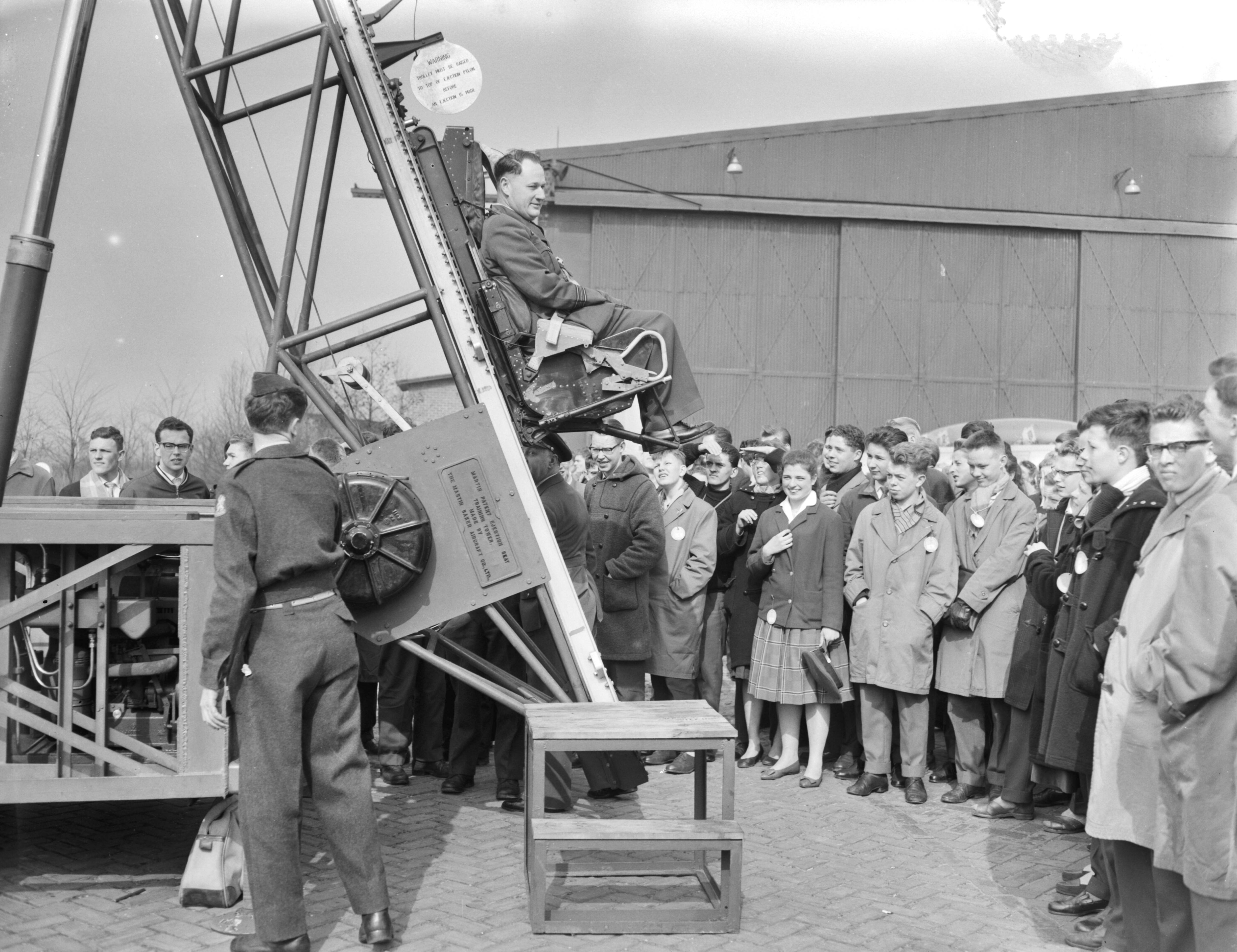 Fotocollectie Anefo — Nationale Luchtvaartdag op Soesterberg. Majoor M. E. J. A. Smitshuysen , hoofd LVD, demonstreert schietstoel — Foto: Rossem, Wim van / Anefo. Licentie: Set B: Rechtenvrij / Publiek Domein. Bron: Nationaal Archief. http://hdl.handle.net/10648/a990b3e6-d0b4-102d-bcf8-003048976d84