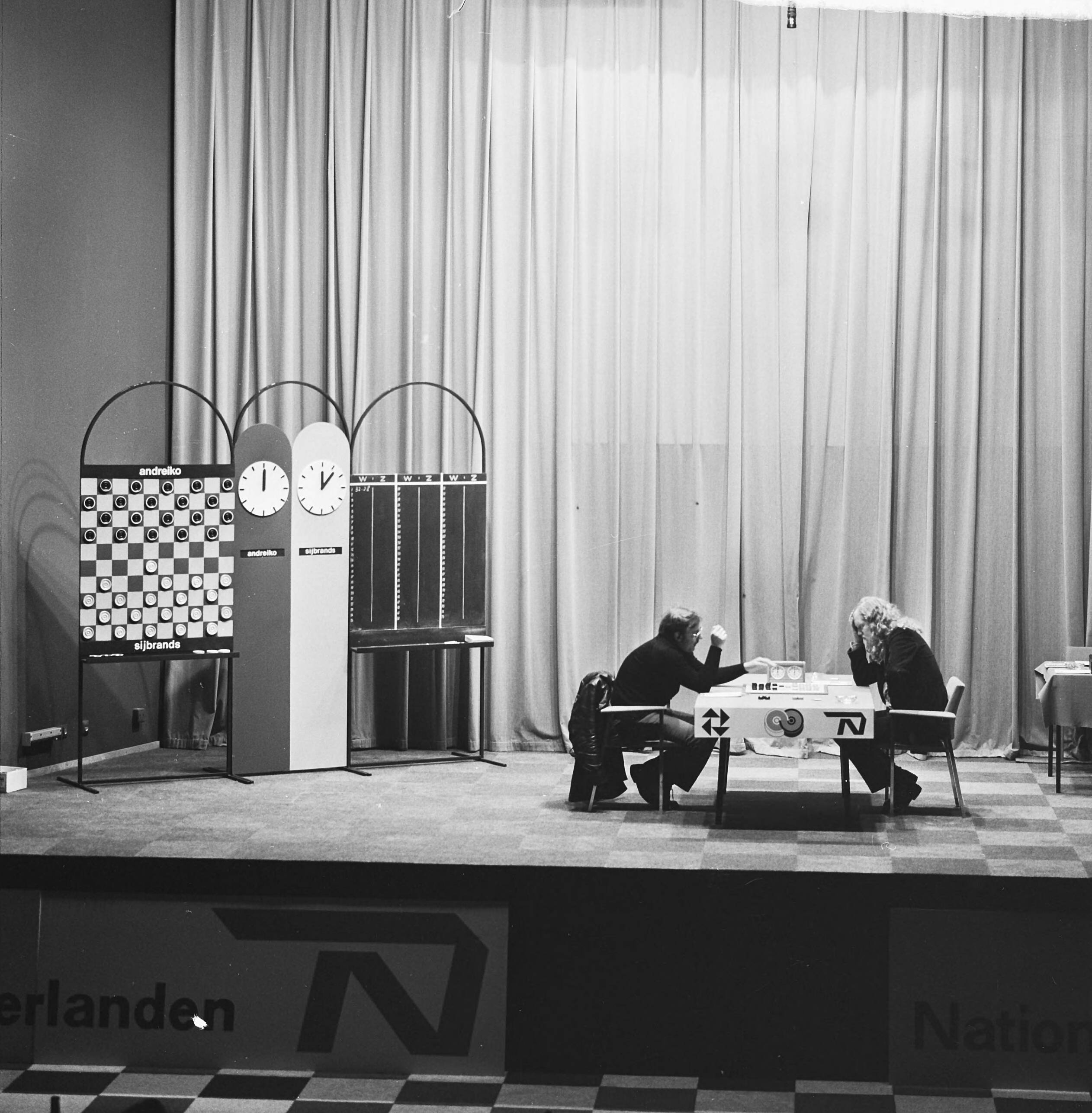 Fotocollectie Anefo — Wereldkampioenschap dammen in Den Haag , Andreiko (links) en Sijbrands tijdens zevende partij — Foto: Mieremet, Rob / Anefo. Licentie: Set B: Rechtenvrij / Publiek Domein. Bron: Nationaal Archief. http://hdl.handle.net/10648/ac394b1c-d0b4-102d-bcf8-003048976d84